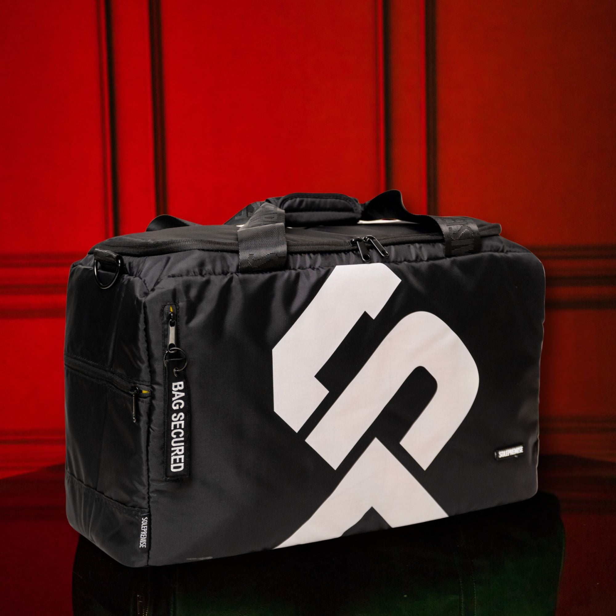 Black duffel bag with a white logo on a red background
