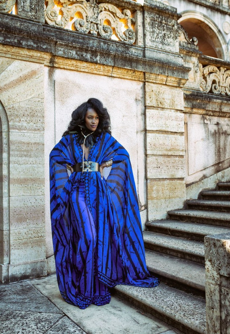 Person wearing a blue and black patterned dress standing on stone steps with ornate architecture.