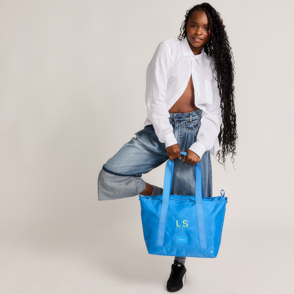 Person holding a blue tote bag with initials on a plain background