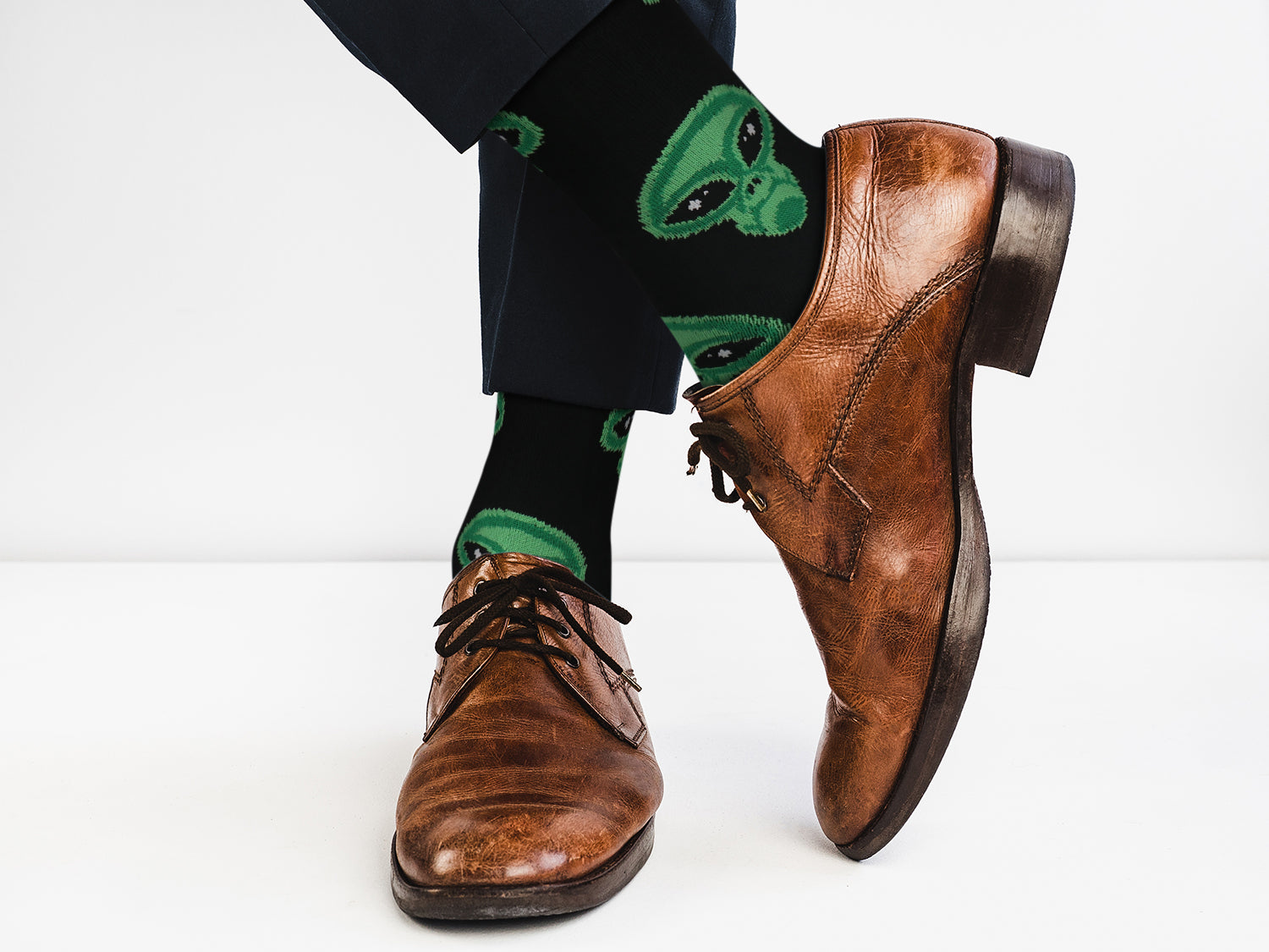 Brown leather shoes with green alien socks on a white background