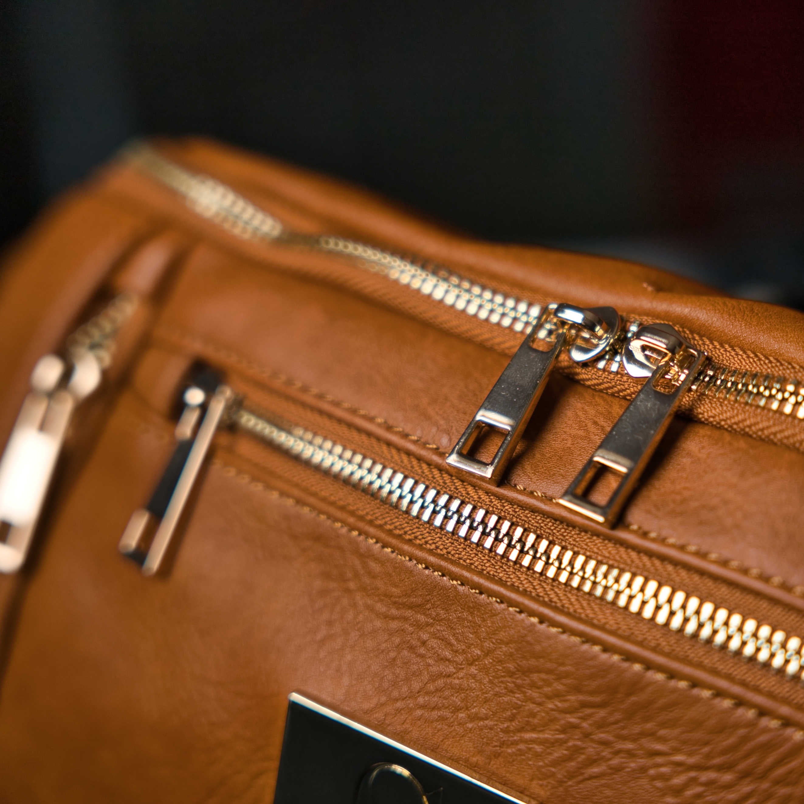 Close-up of a brown leather bag with gold zippers.