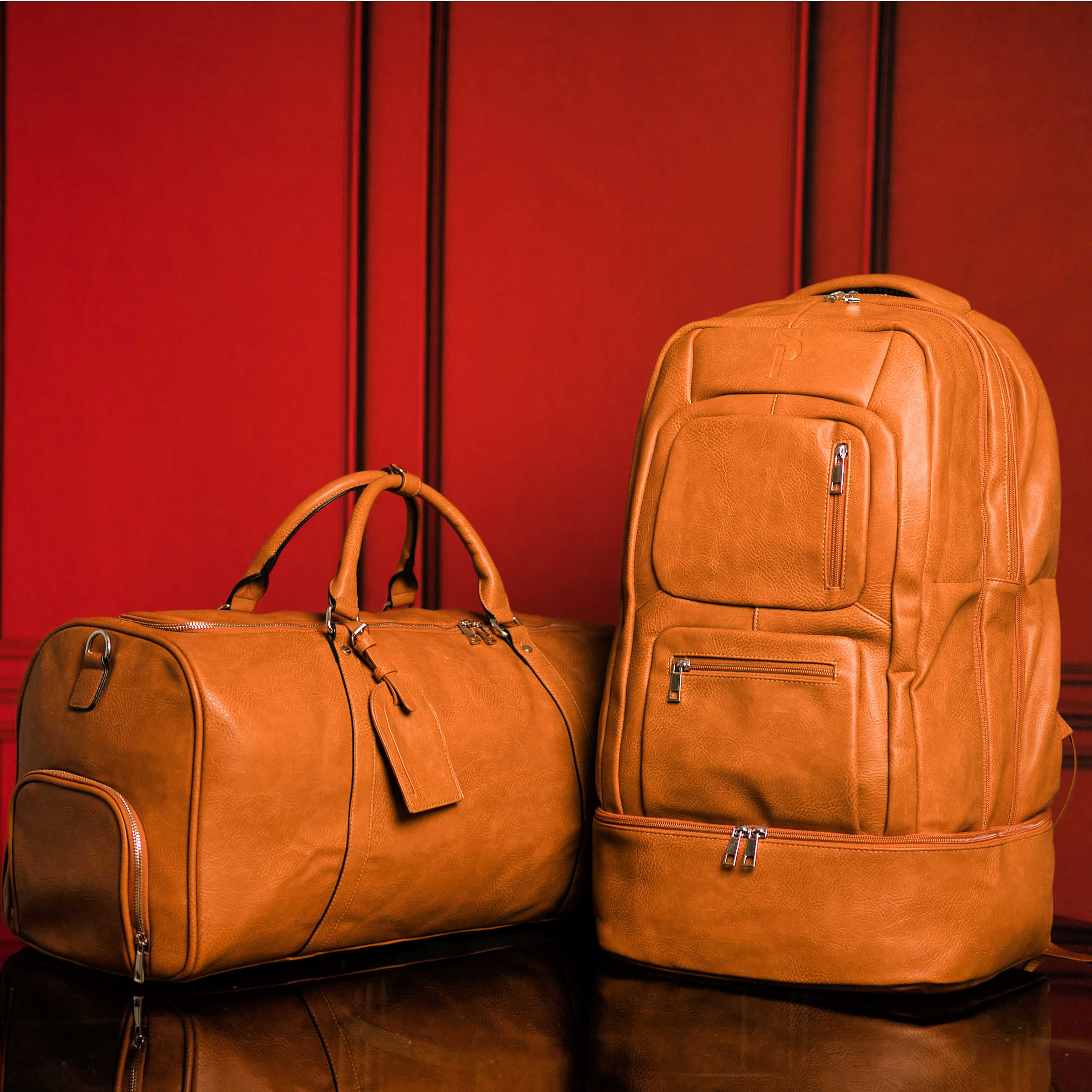 Two brown leather bags, a duffel bag and a backpack, against a red background.