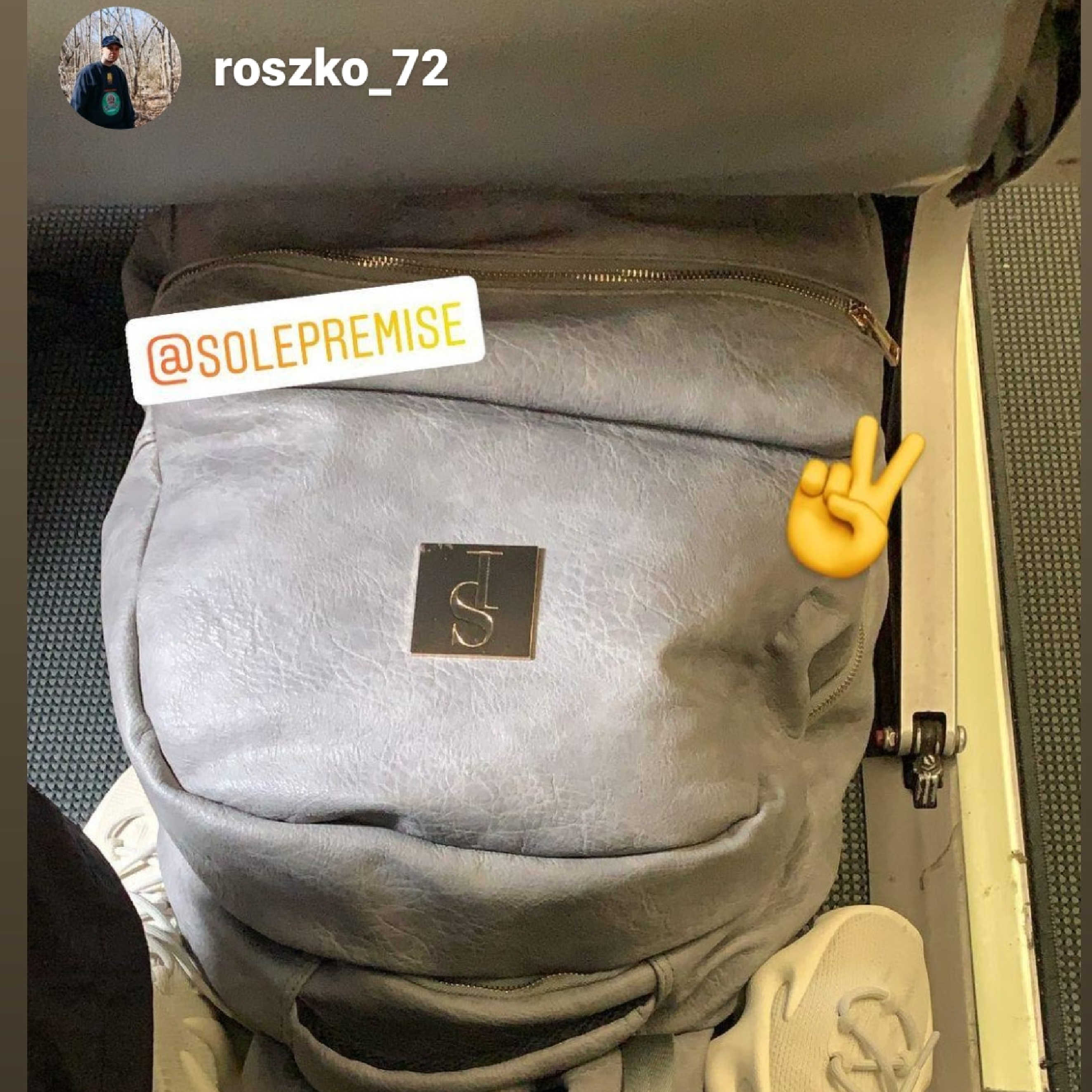 Gray backpack with visible branding and a peace sign emoji on a textured surface.