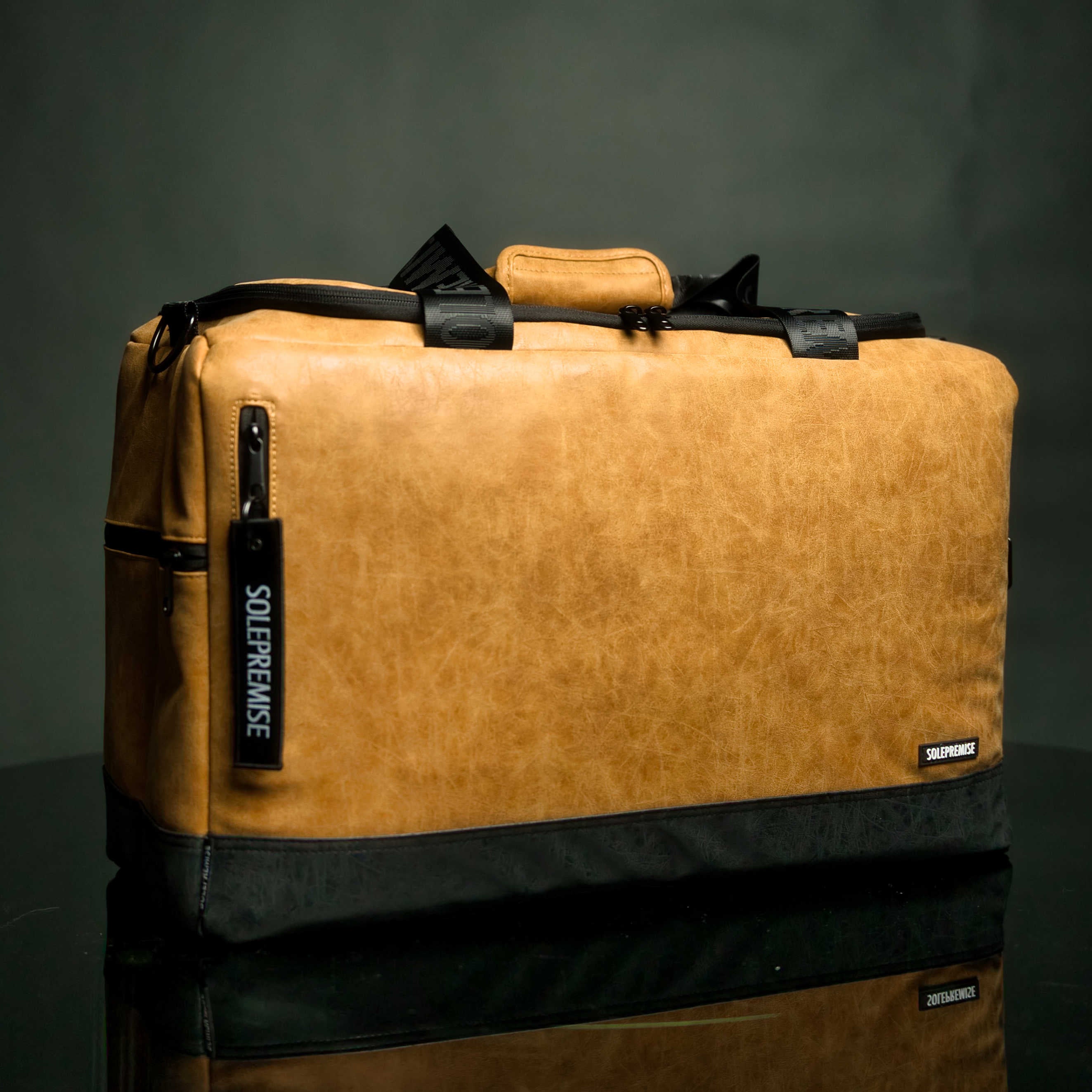 Brown leather bag with black accents on a reflective surface and dark background