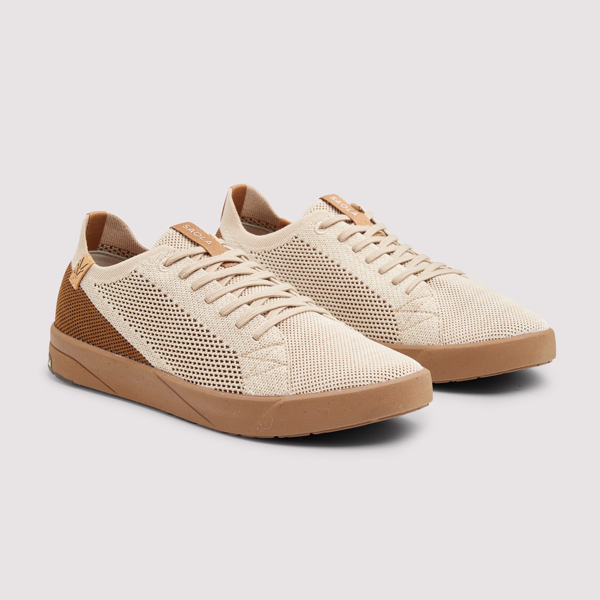 A pair of beige knit sneakers with brown mesh side panels and gum soles, displayed on a light gray background.