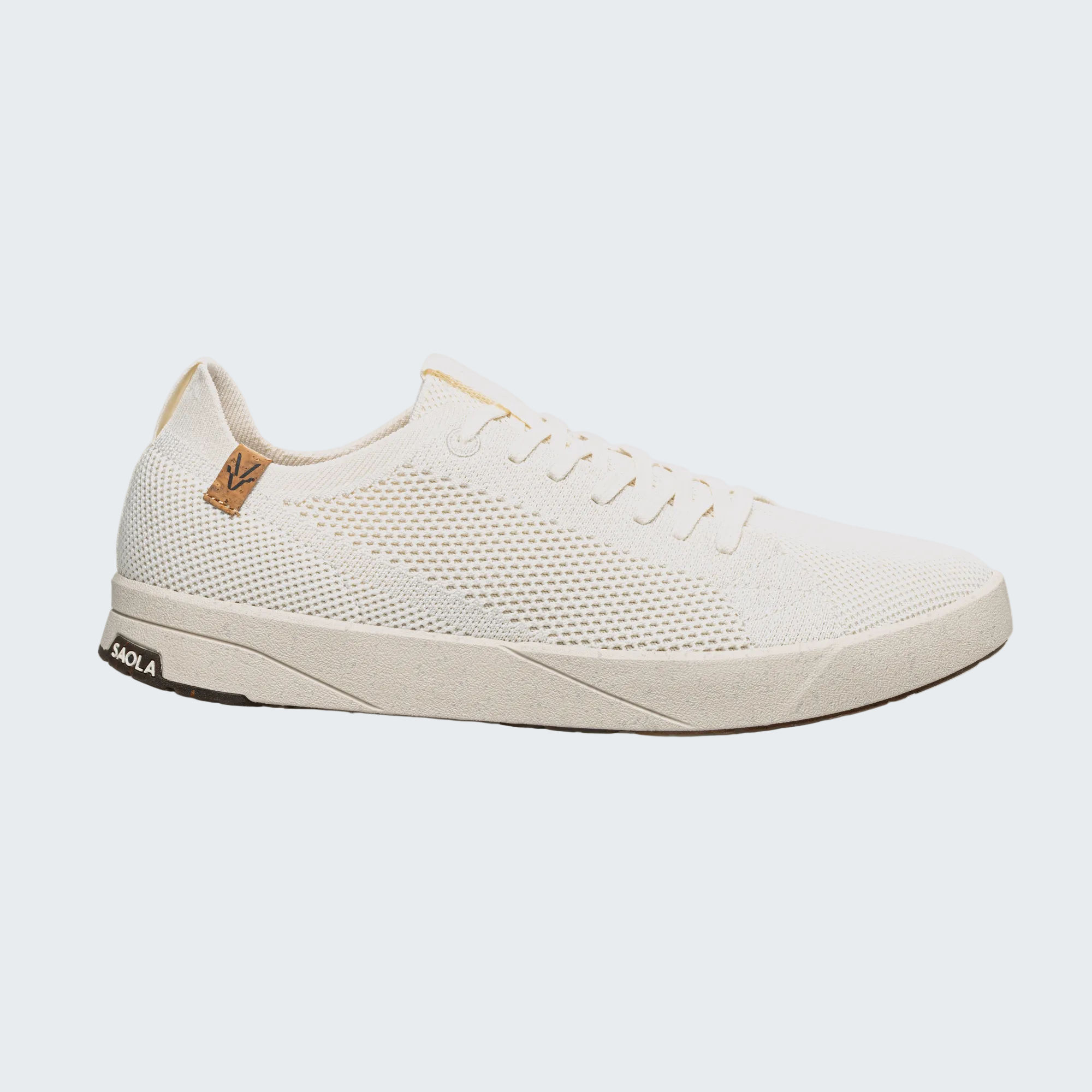 A white knit sneaker with a textured mesh upper, white laces, and a white sole, featuring a small tan leather heel tab with a 'V' logo and a black 'VOLA' brand tag on the heel.
