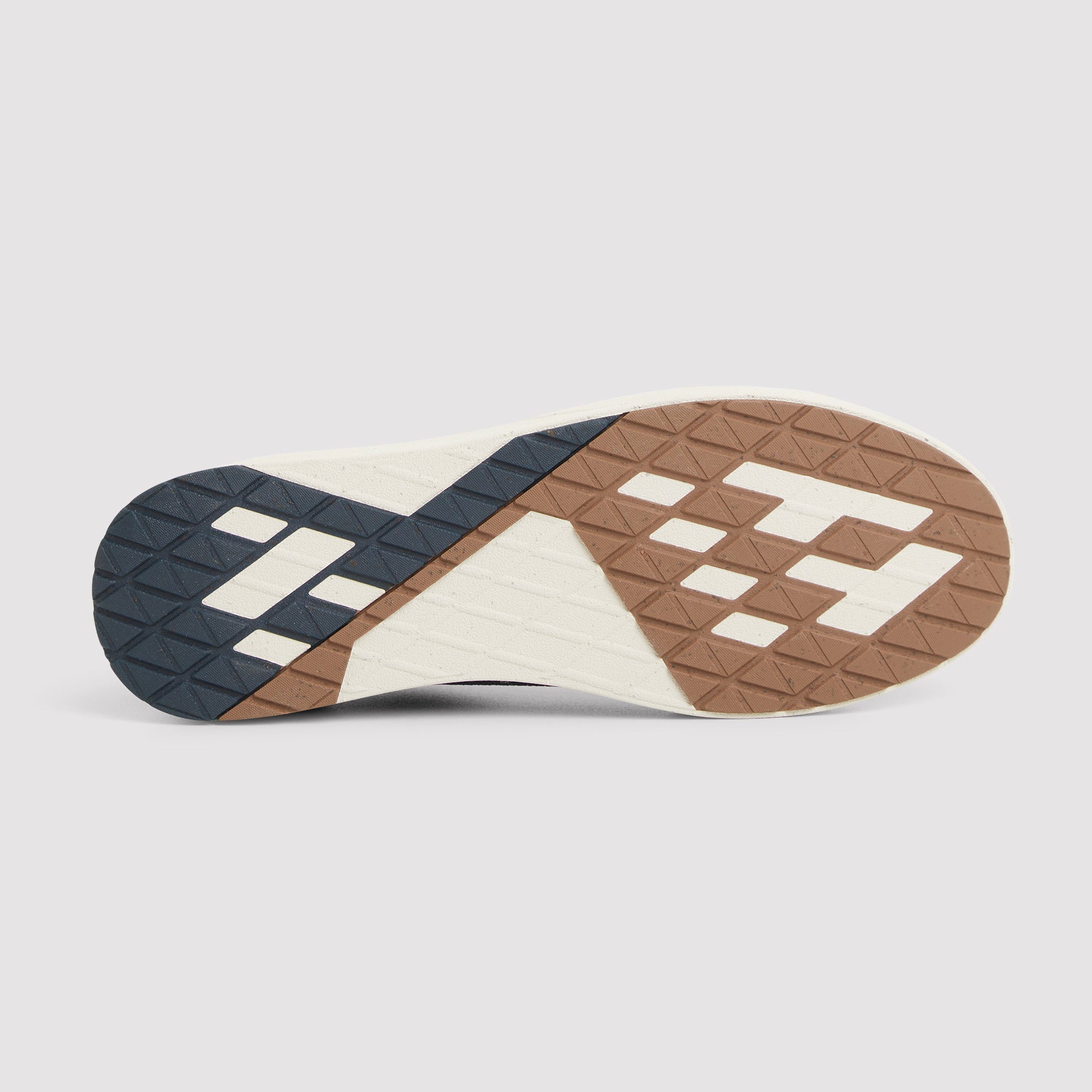 The outsole of a sneaker shown from a top-down view, featuring a geometric pattern of dark navy, brown, and off-white rubber blocks with a textured tread design, set against a light gray background.