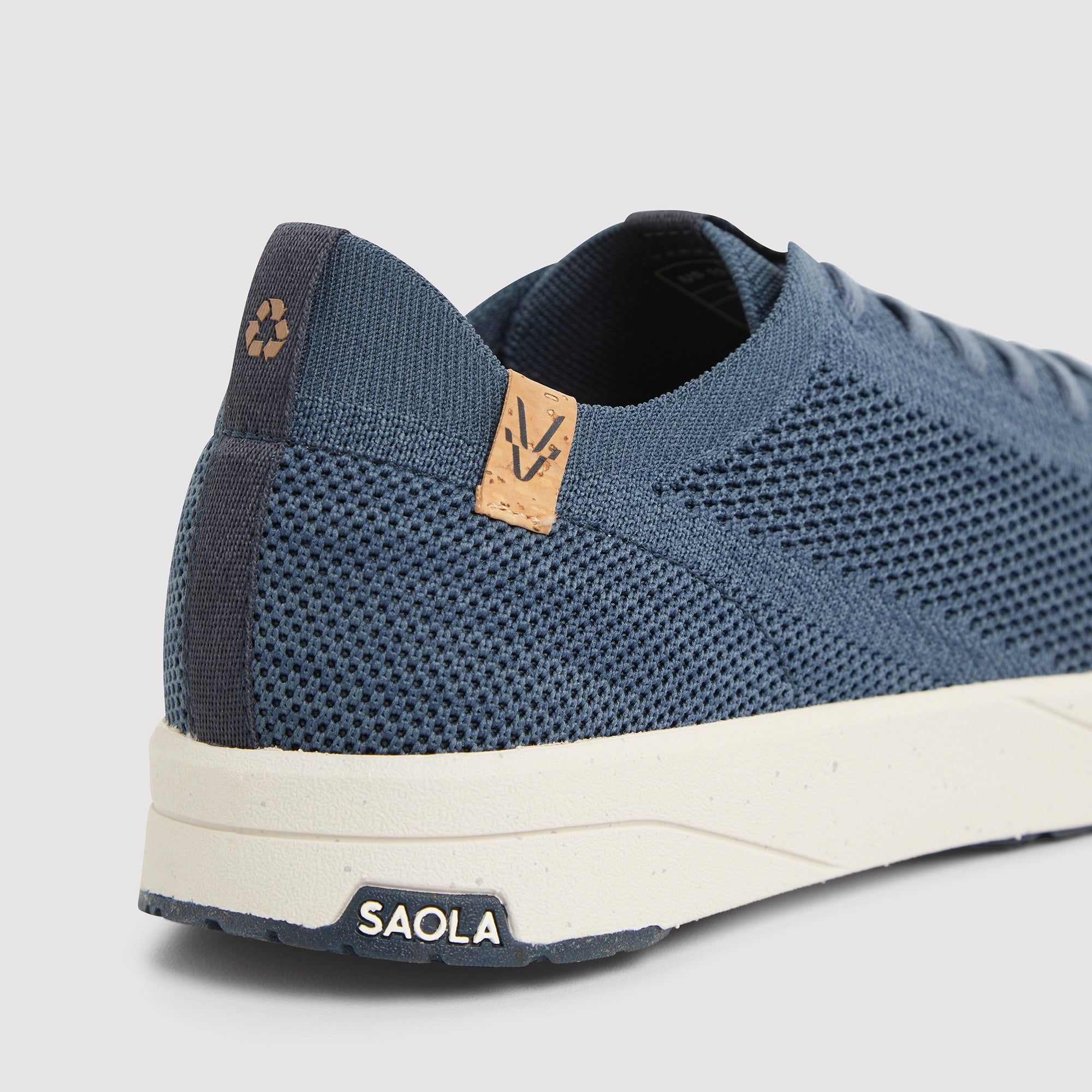 Close-up rear-quarter view of a blue knit sneaker with a white sole, showing the heel, lace area, and SAOLA branding on the outsole.