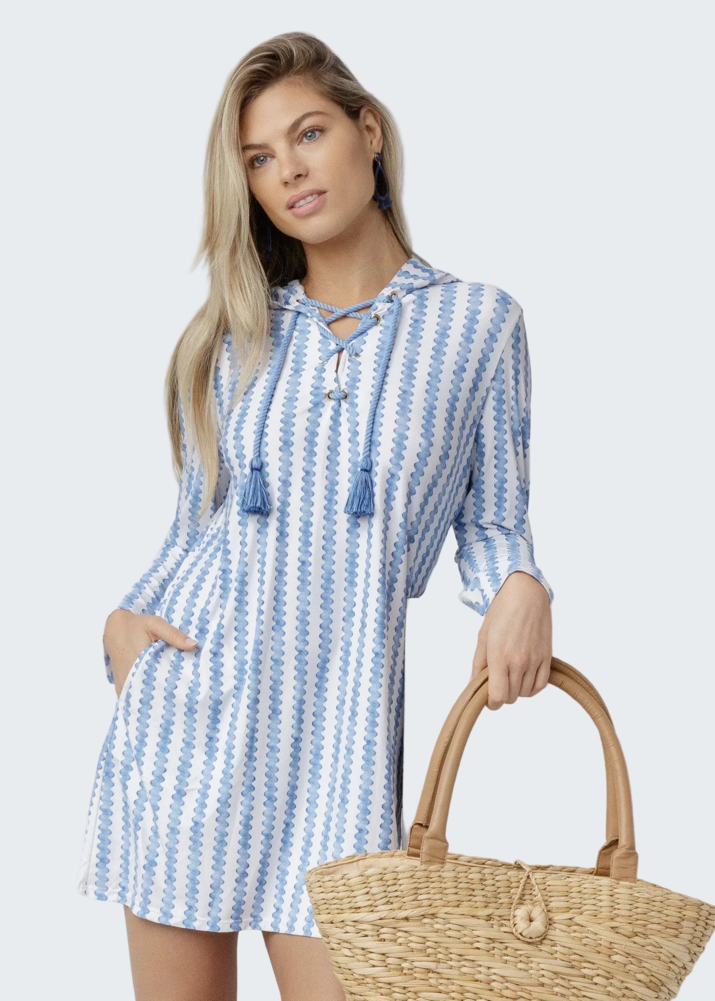 Woman wearing a blue and white striped dress holding a straw bag against a white background