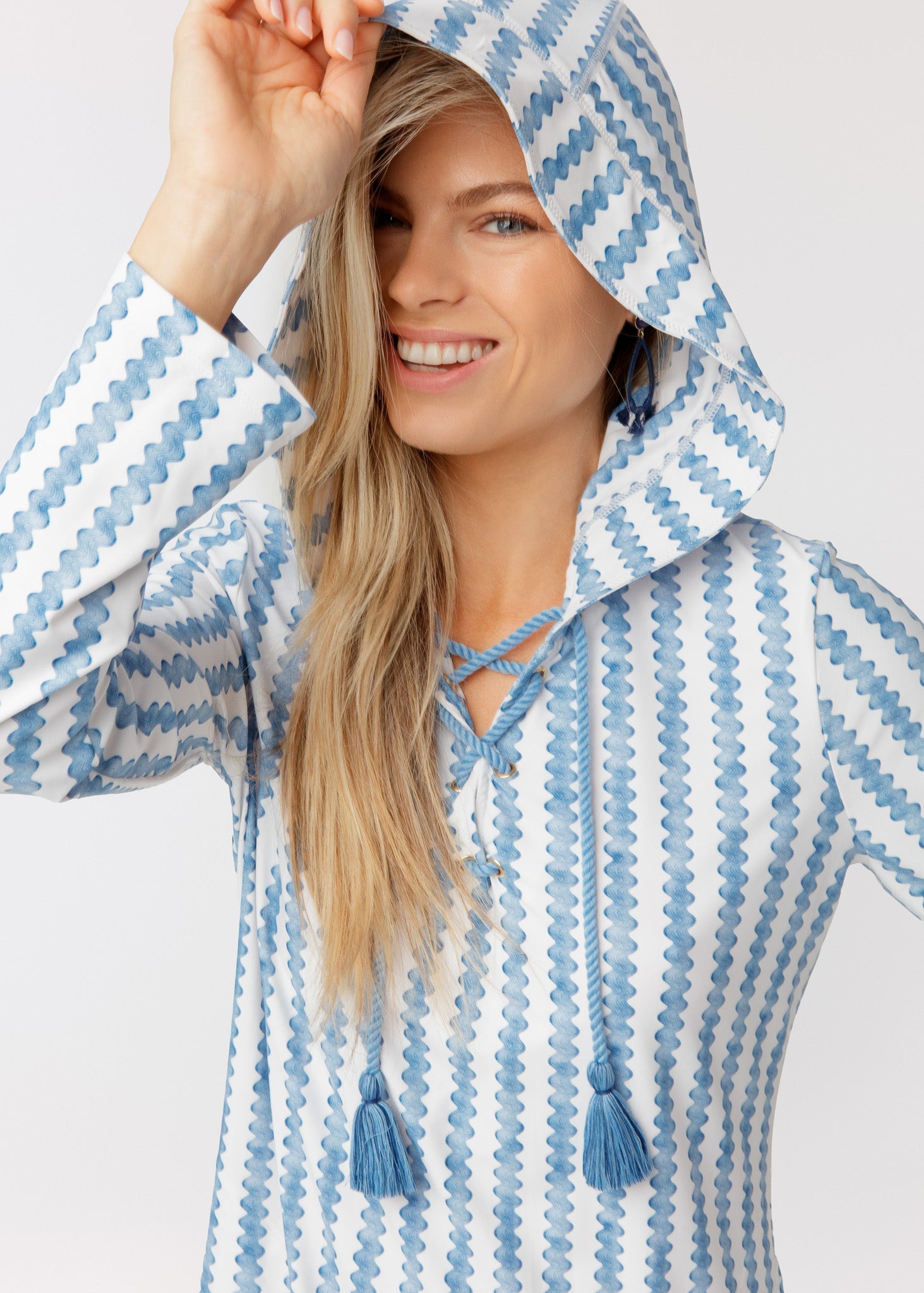 Woman wearing a blue and white patterned raincoat with tassels on a light gray background