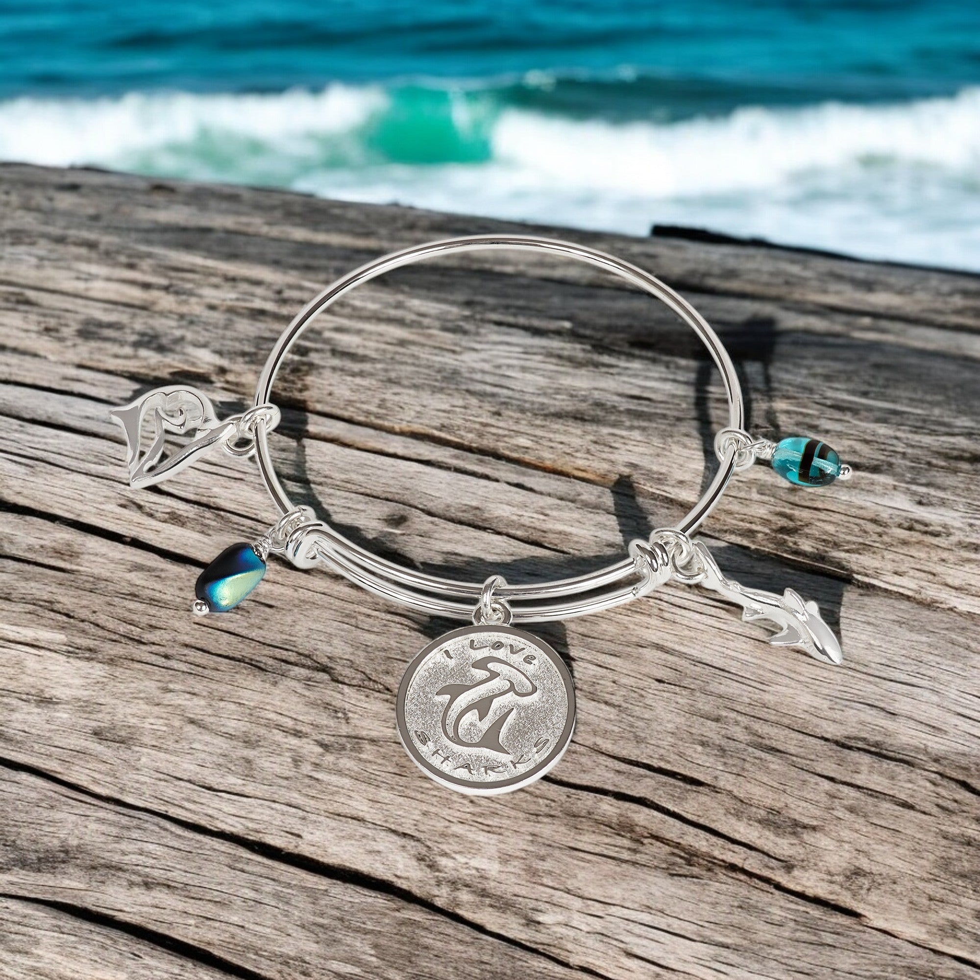 Silver bracelet with charms on a wooden surface with ocean in the background