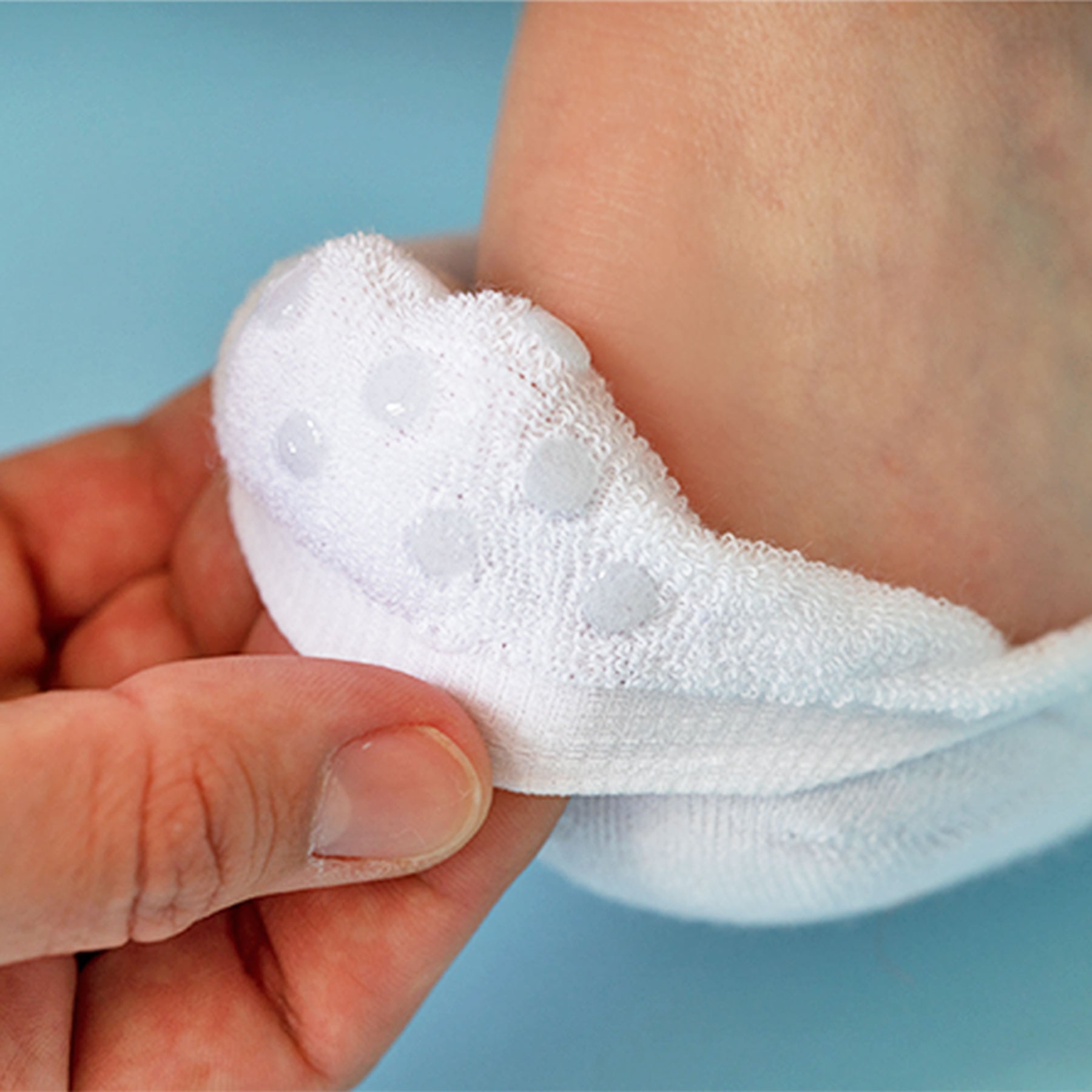 White sock with a textured sole held by a hand against a blue background