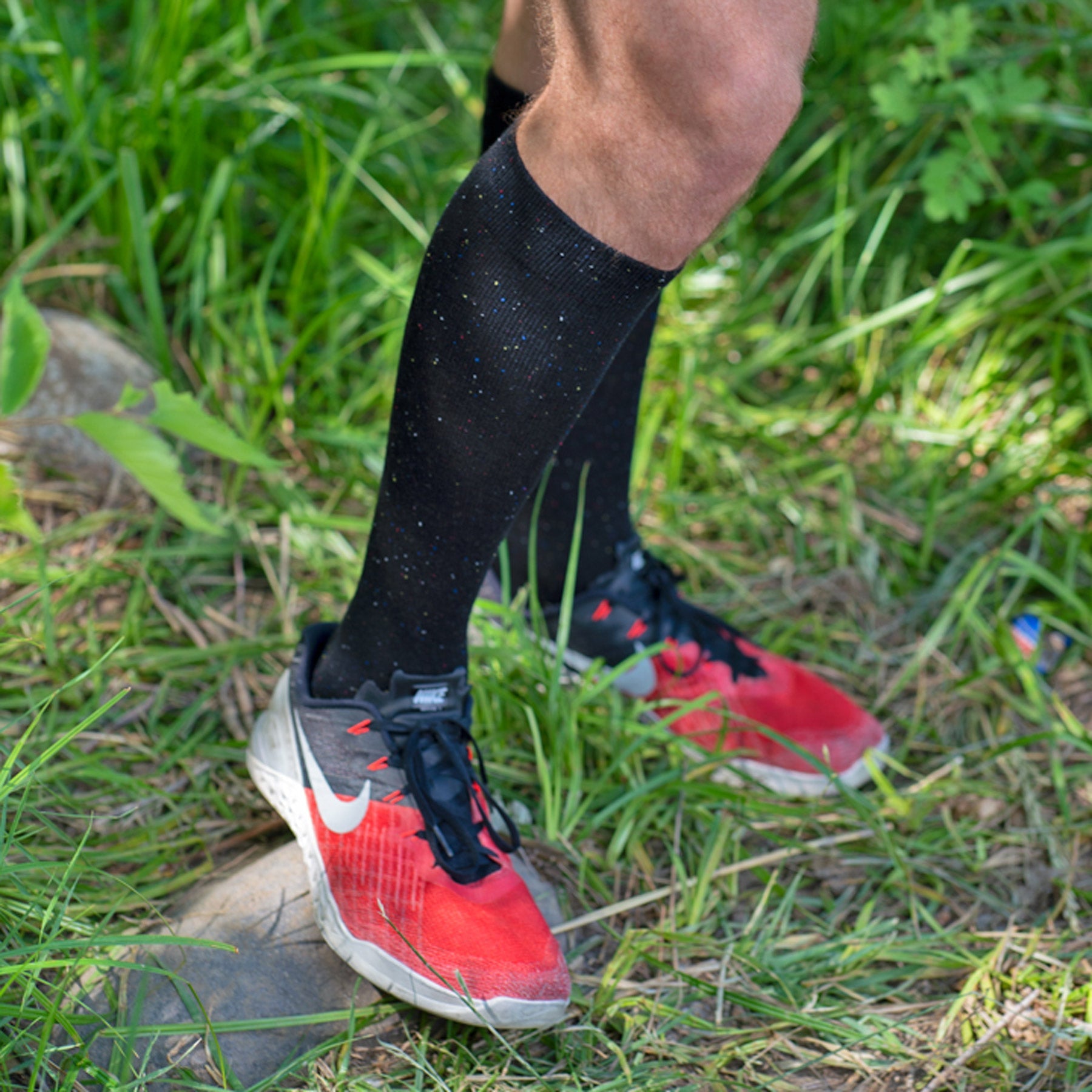 Person wearing red athletic shoes and black socks standing on grass