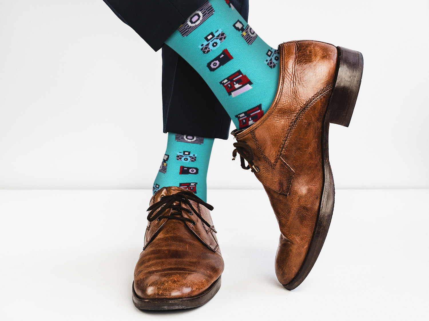 Teal socks with cassette tape design worn with brown dress shoes on a white background