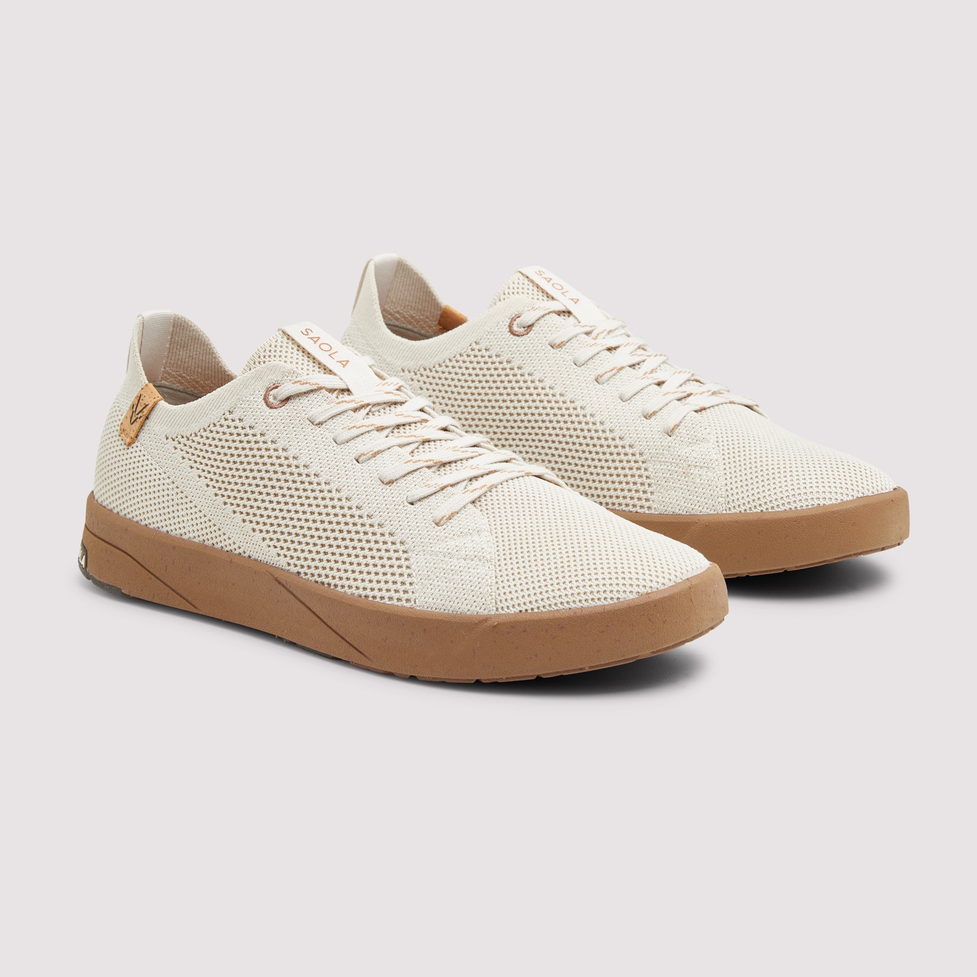 A pair of low-top sneakers in off-white mesh fabric with tan rubber soles, shown on a light gray background.