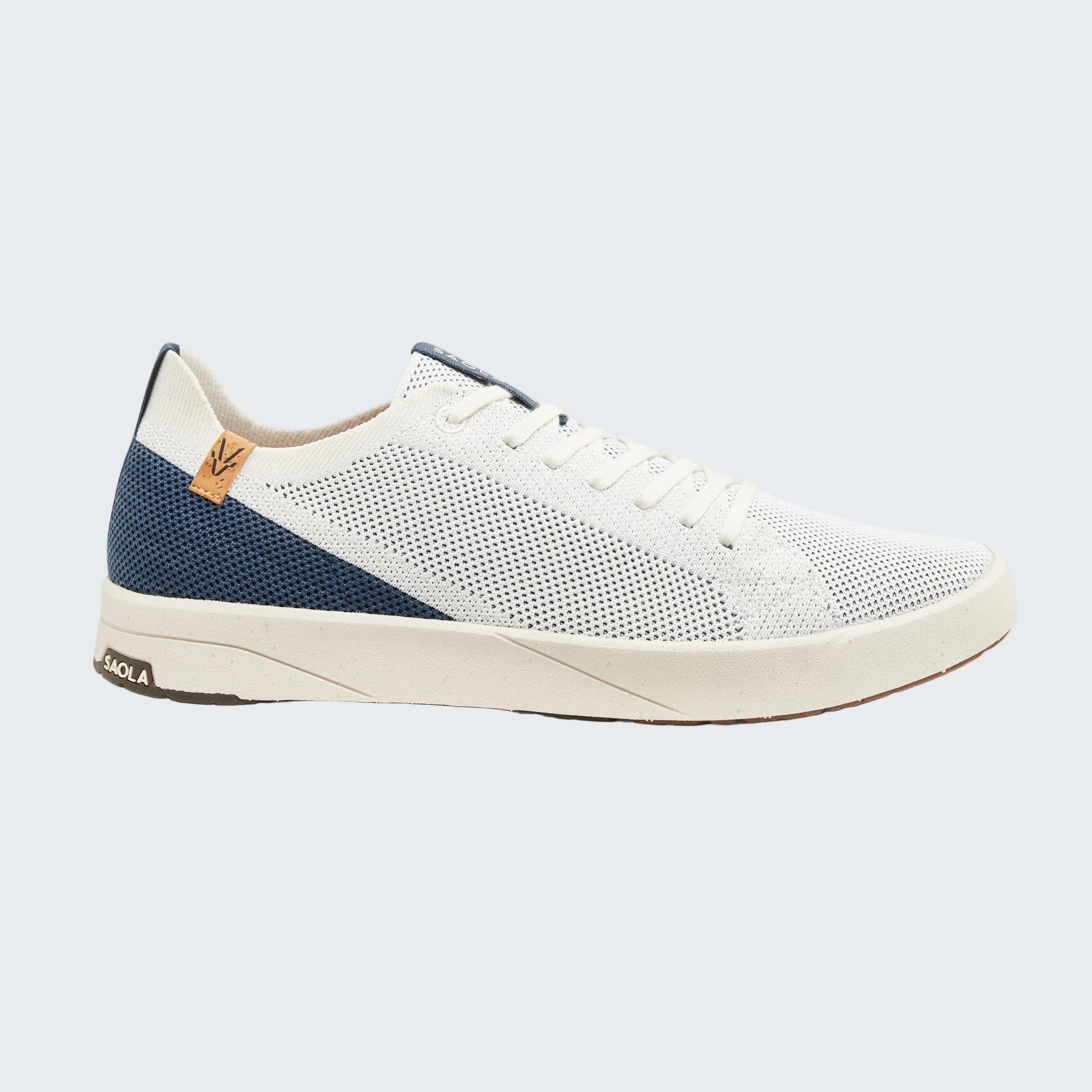 A low-top sneaker shown in a side profile view against a light gray background. The shoe features a white mesh upper, white laces, a navy blue heel panel, and a cream-colored sole.