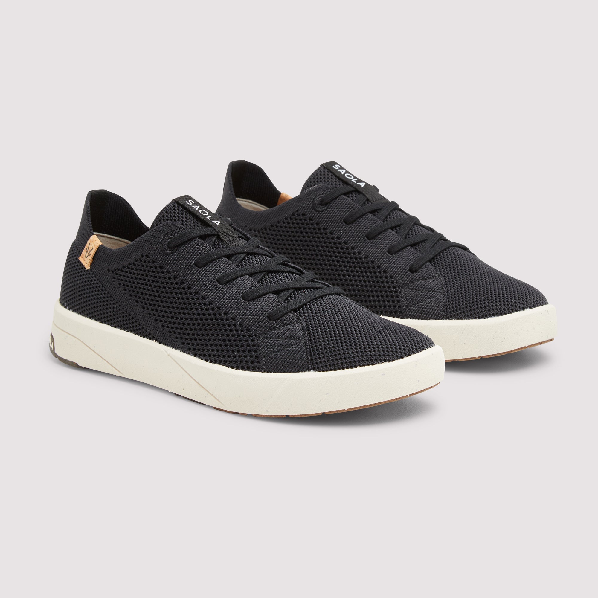 A pair of black mesh low-top sneakers with off-white soles and a small gold brand tag on the side, displayed against a light gray background.