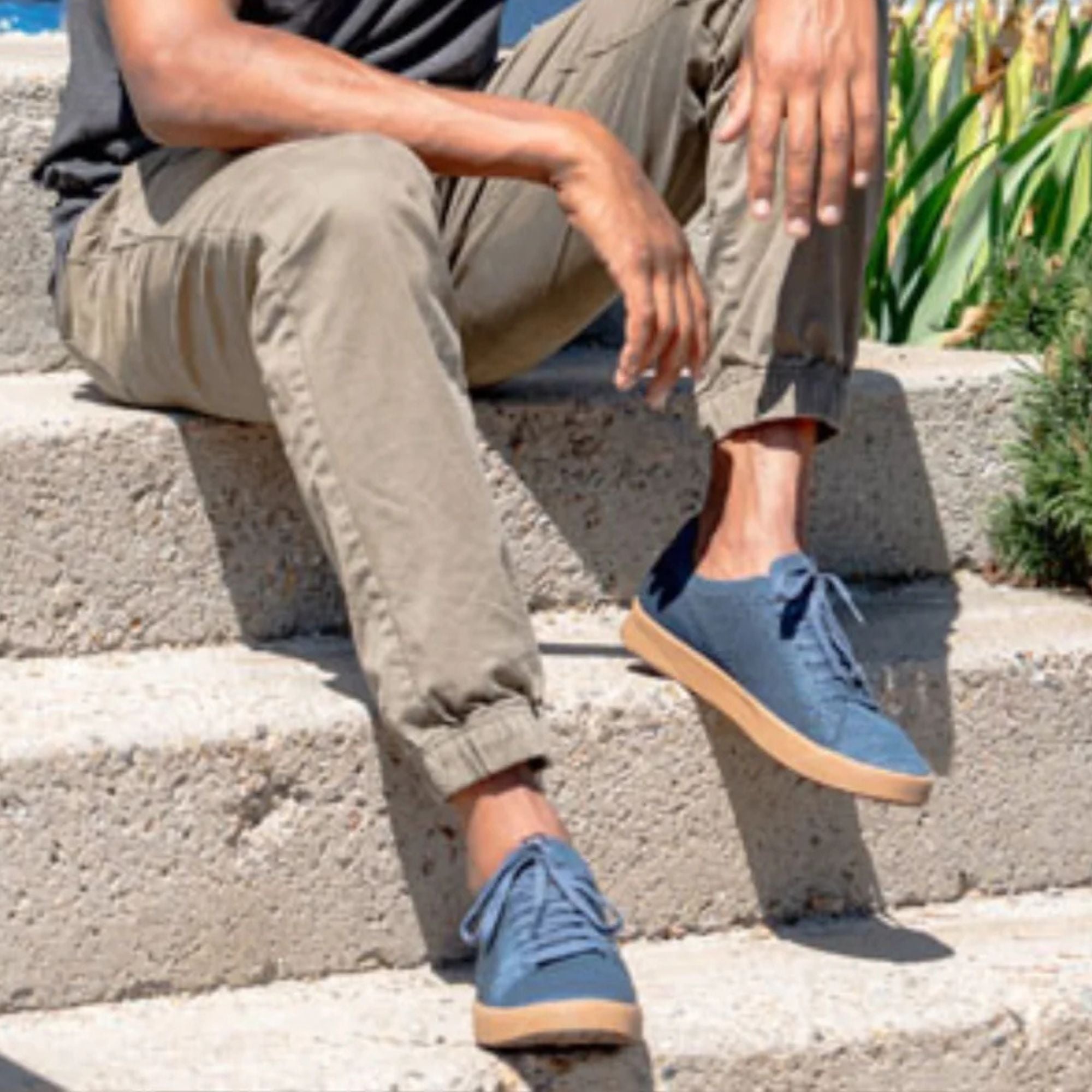 A person sitting on outdoor concrete steps wearing blue low-top sneakers with tan soles and olive cargo pants.