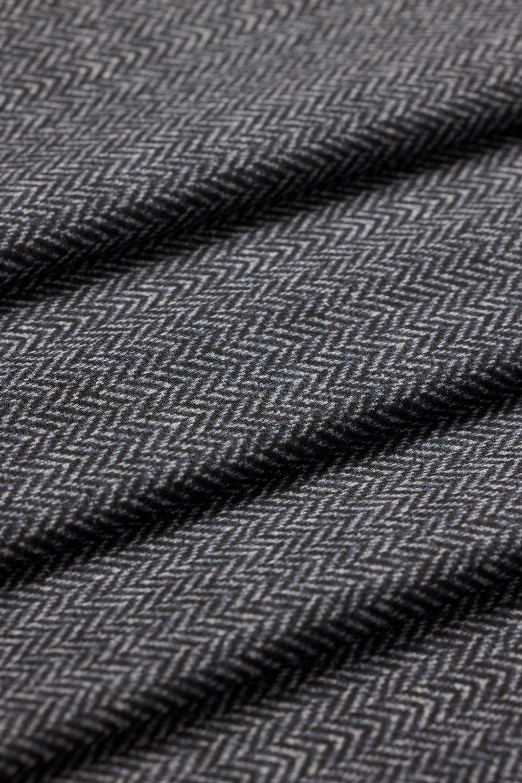 Close-up of a dark gray and black herringbone woven fabric with a textured chevron pattern and soft diagonal folds.