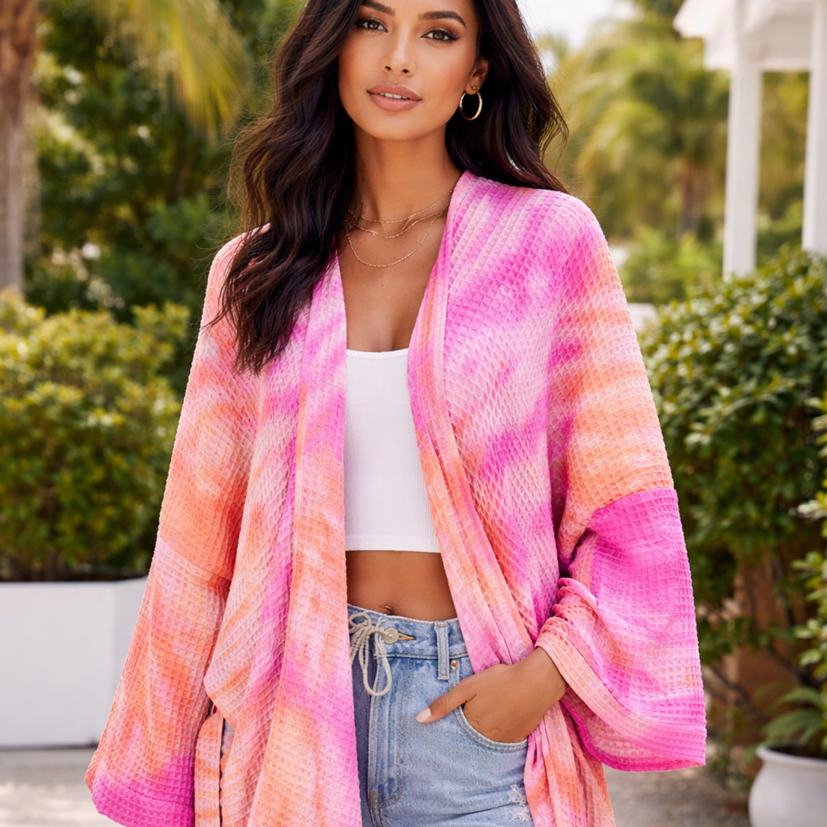 Woman wearing a pink and orange striped kimono with a white top and denim shorts outdoors.