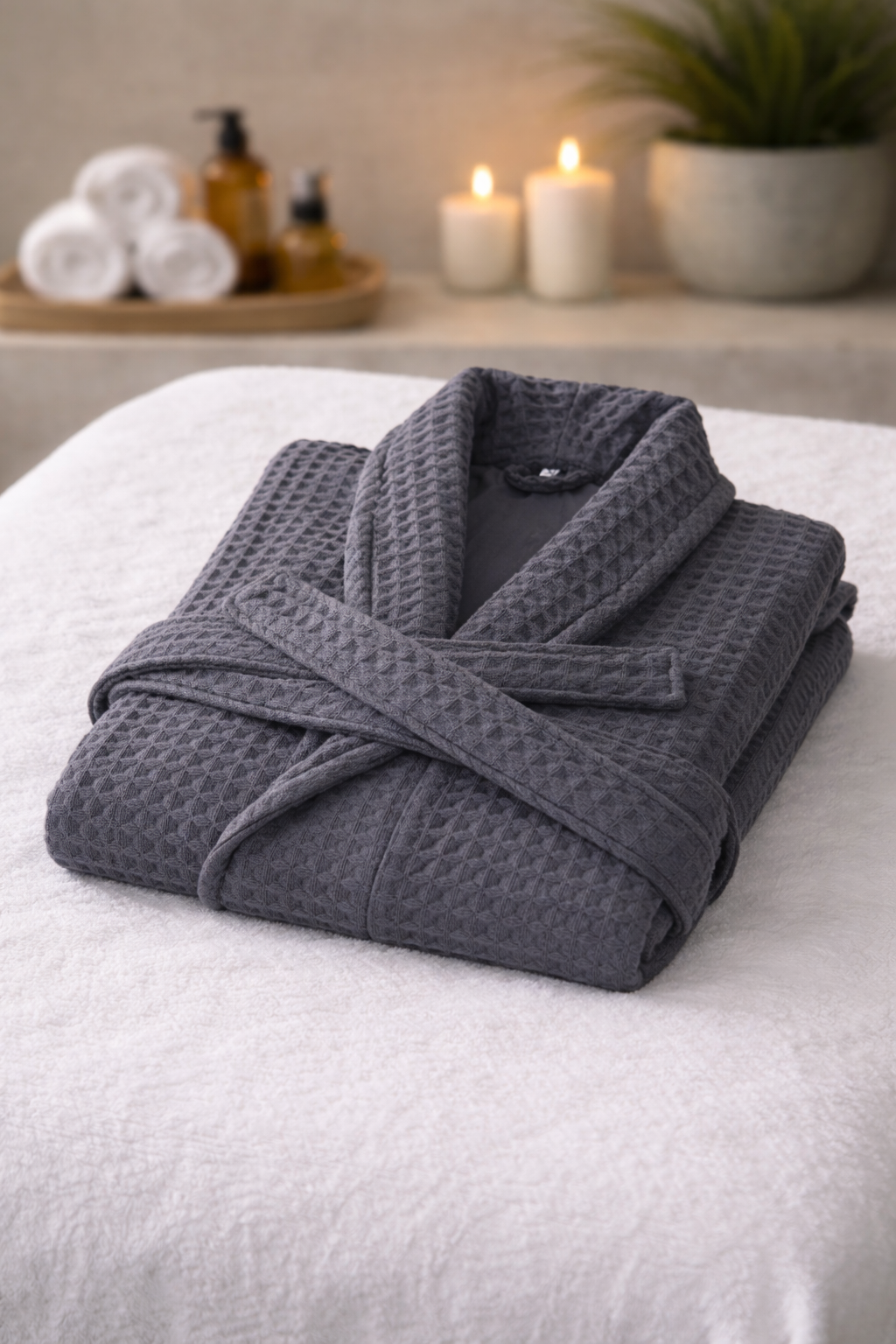 Folded gray robe on a white surface with candles and towels in the background