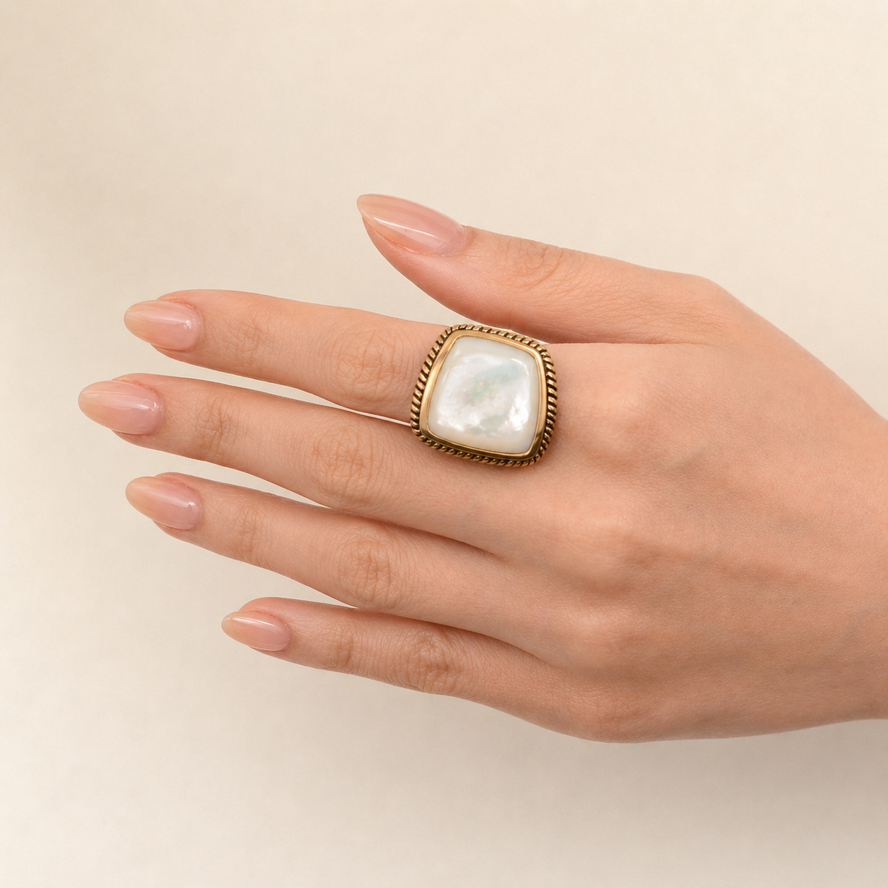 Hand wearing a gold ring with a large pearl on a beige background