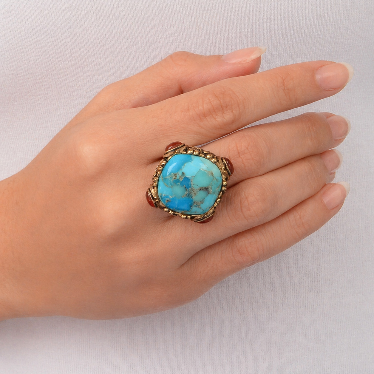 Hand wearing a turquoise ring with gold band on a light gray background