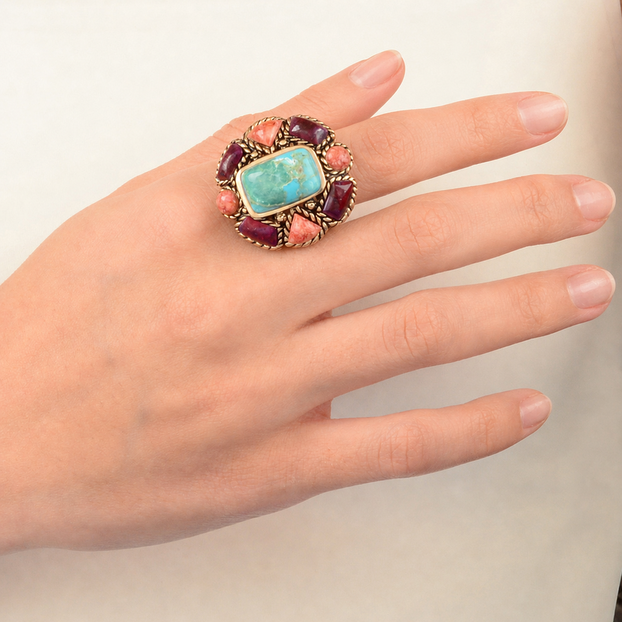 Hand wearing a colorful ring with a turquoise stone on a plain background
