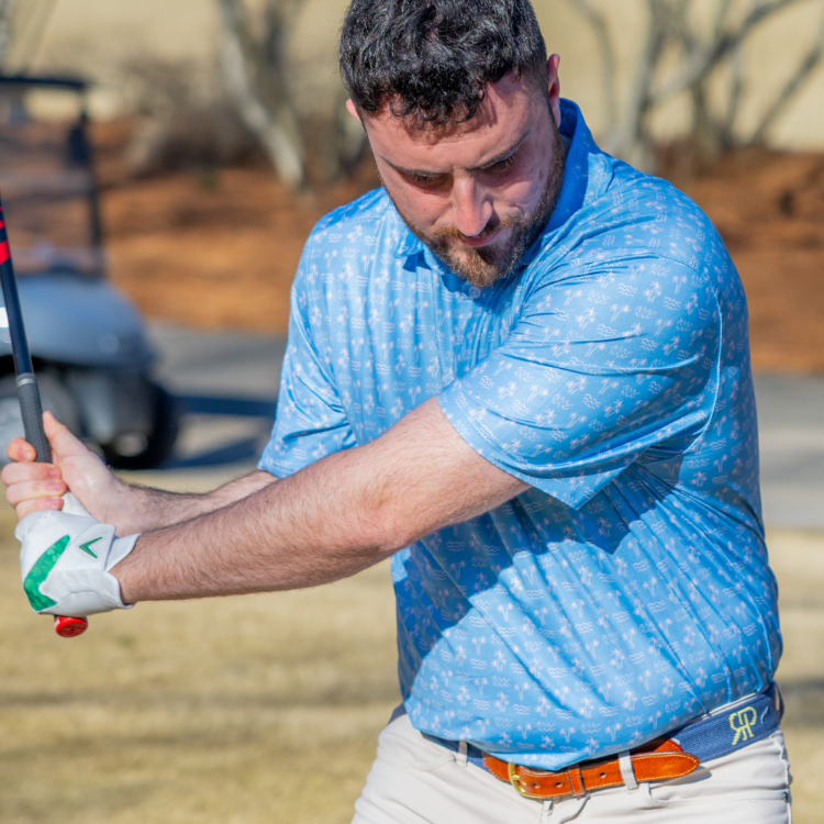 Man in a blue shirt swinging a golf club on a golf course