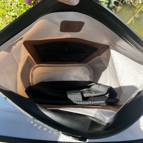 Close-up of a kayak seat with a black cover and brown cushion, held above water.