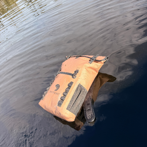 Orange dry bag floating on water with a visible brand logo.