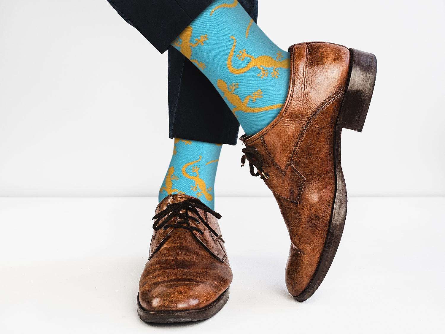 Blue socks with yellow lizard design worn with brown dress shoes on a white background