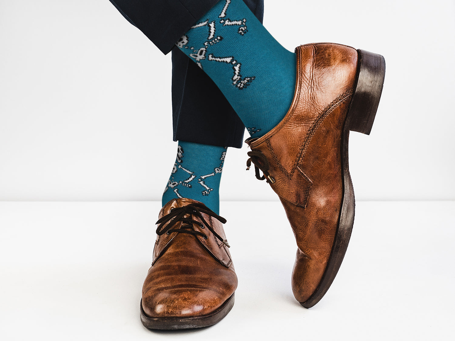 Brown dress shoes and teal socks with a pattern worn by a person on a white background