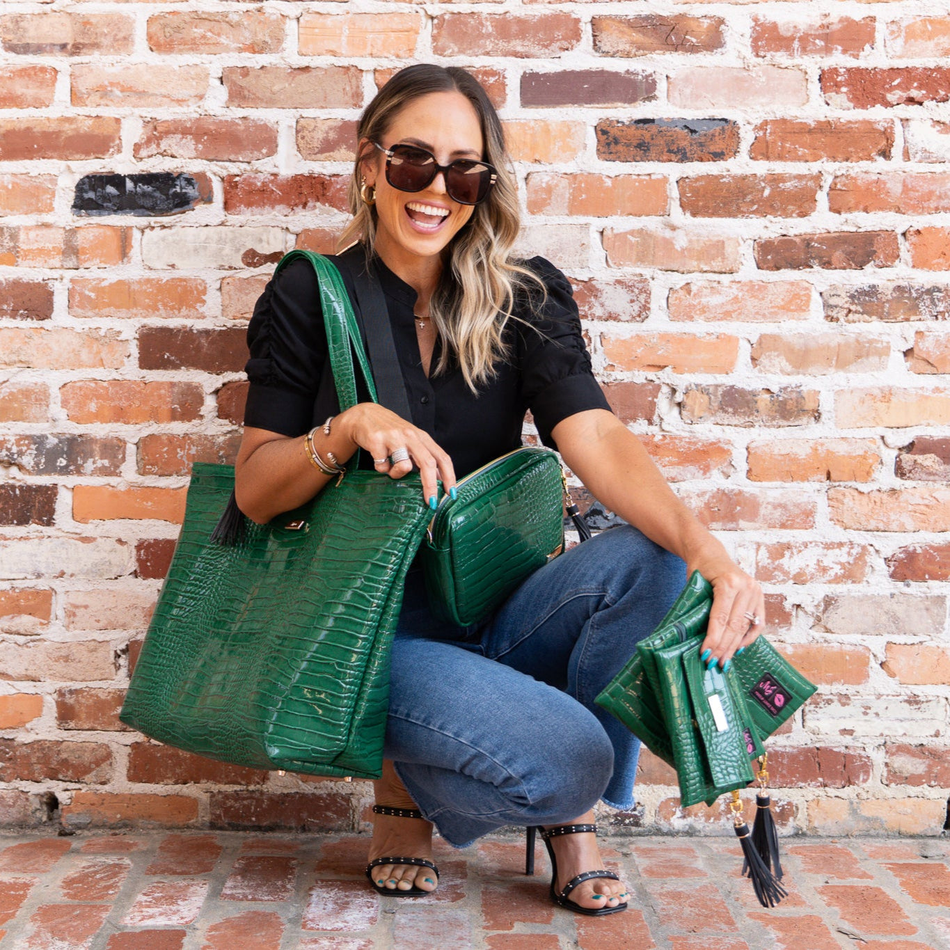 Woman holding multiple green handbags against a brick wall