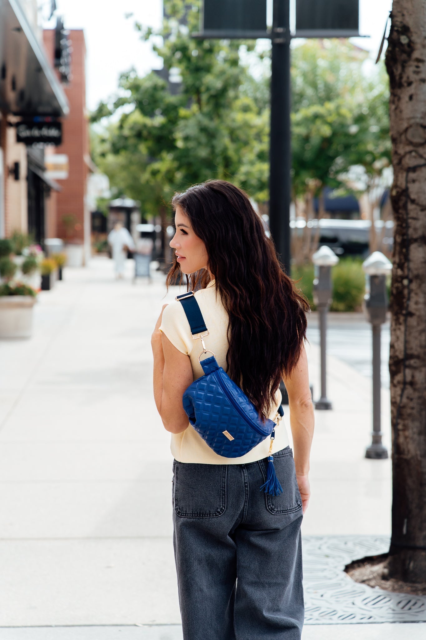 Woman with a blue crossbody bag walking on a sidewalk