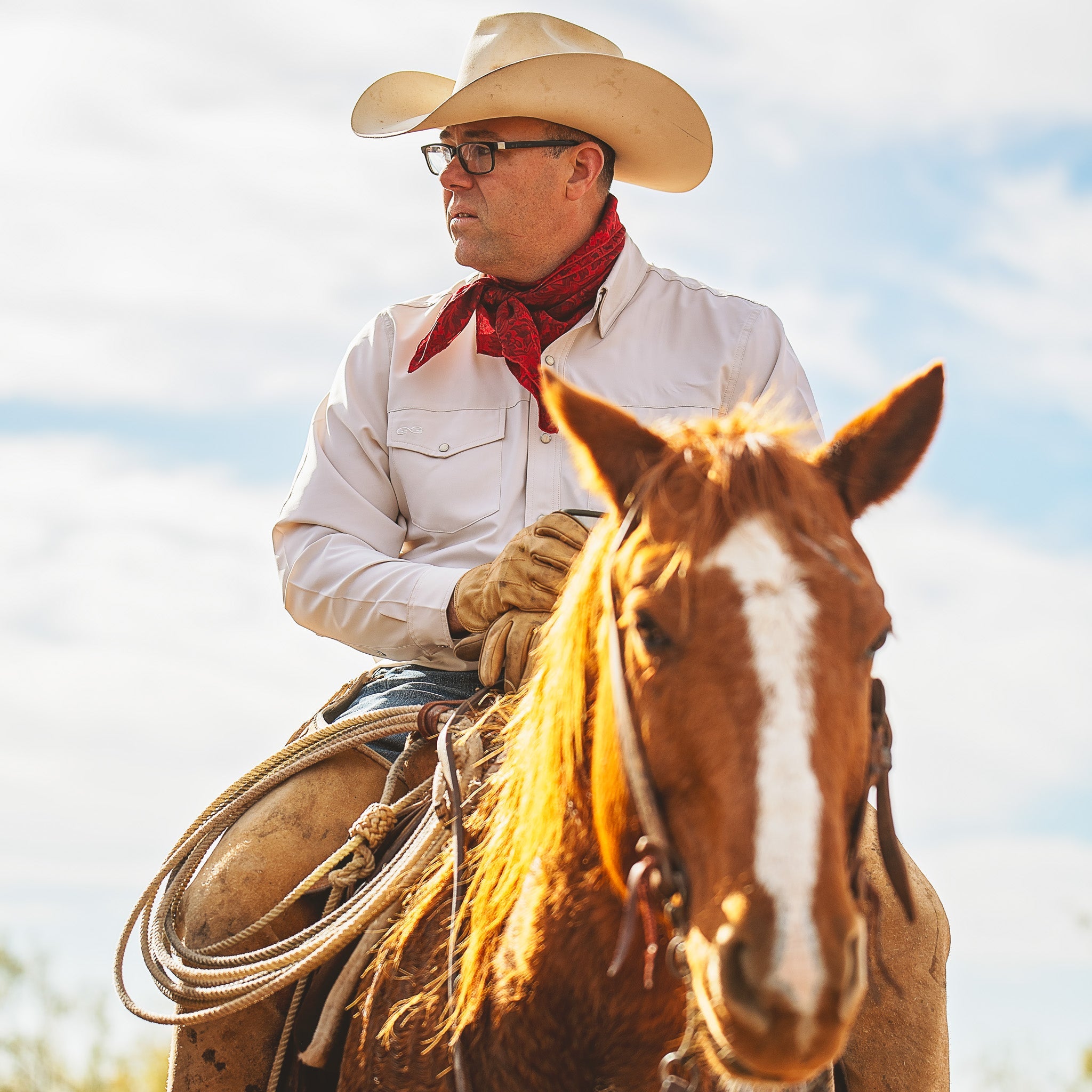Man in cowboy hat and scarf riding a horse with a clear sky background