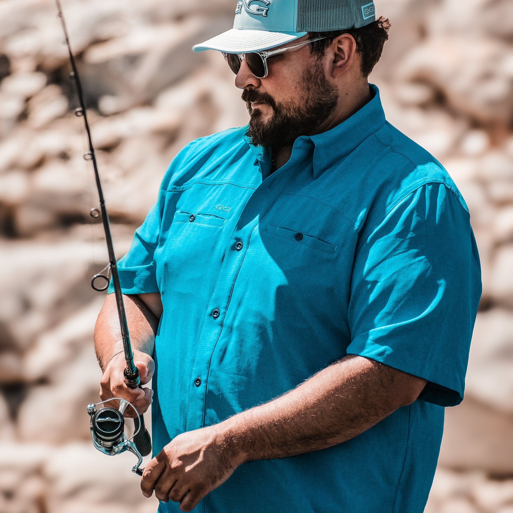Man in blue shirt and cap holding a fishing rod with a blurred natural background