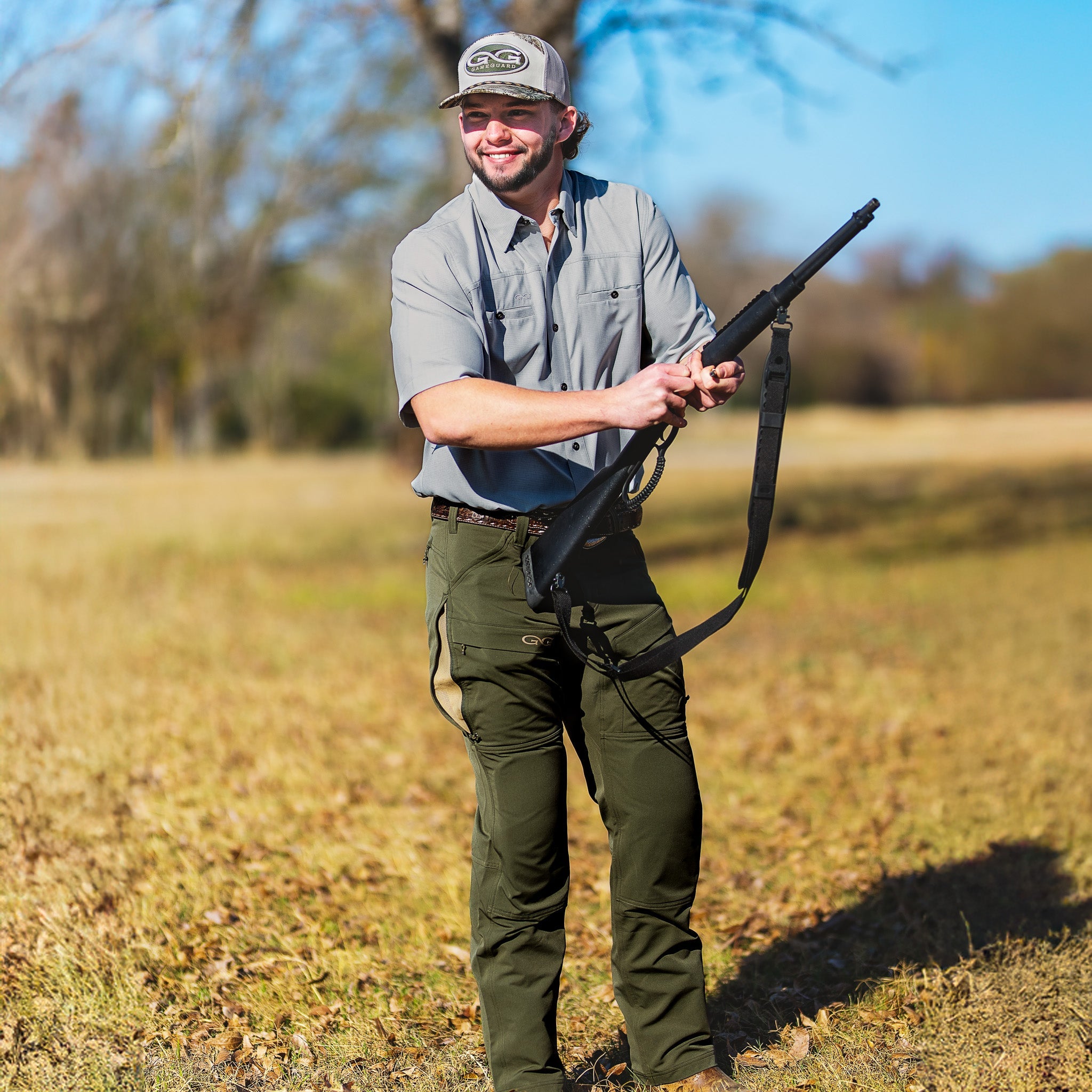 Man holding a rifle in a field with trees in the background