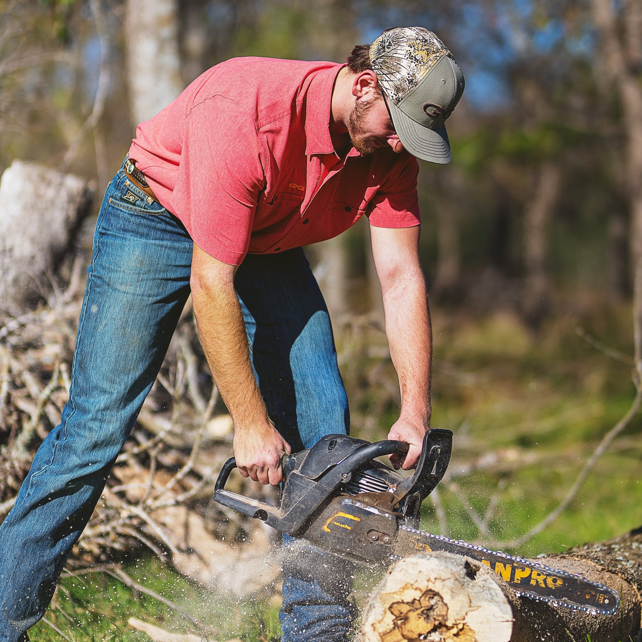 Man using a chainsaw to cut wood in a forest setting