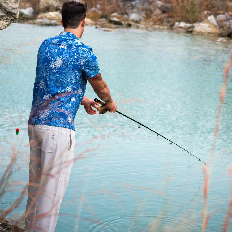Man fishing in a clear blue lake with a rocky shoreline