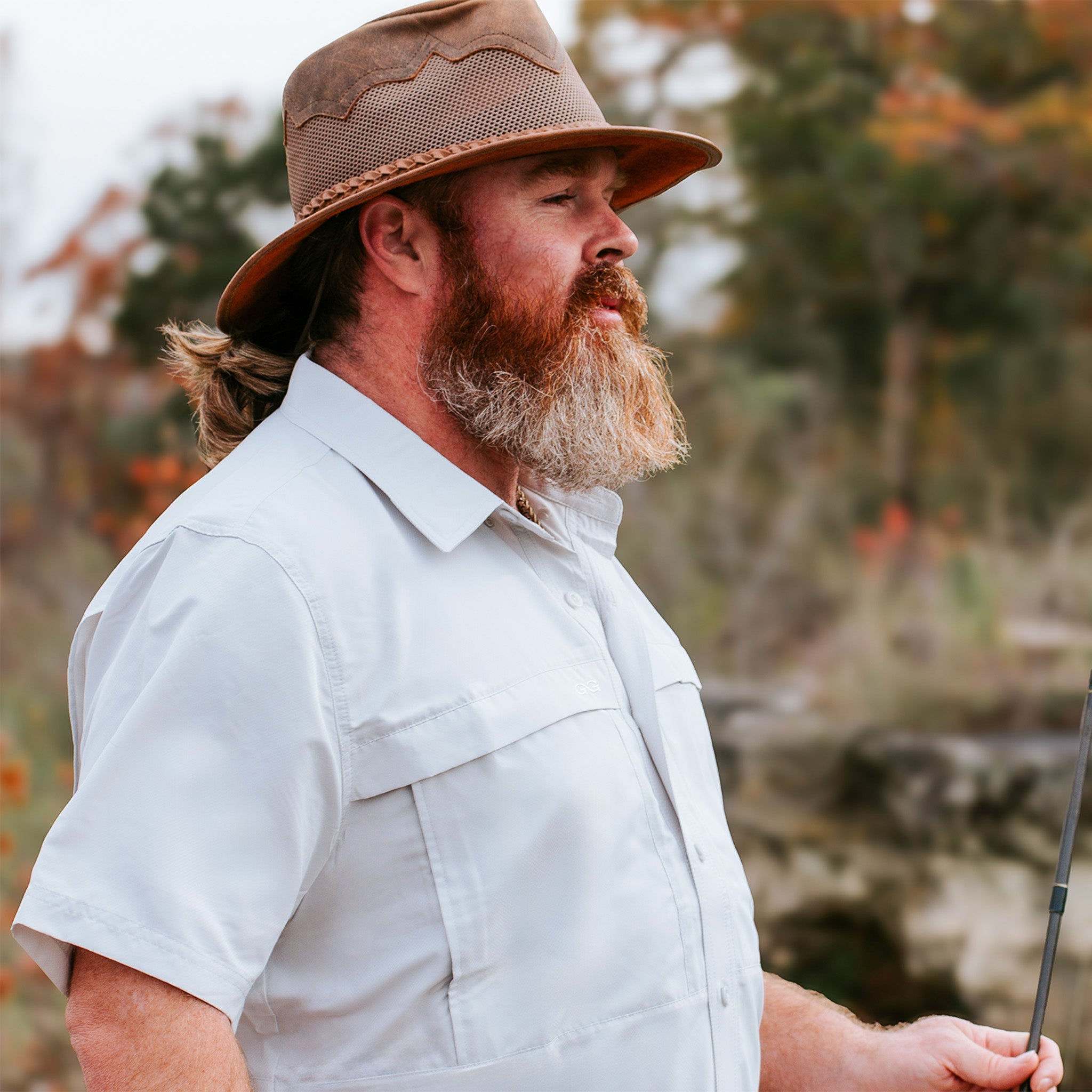 Man with a beard wearing a brown hat and light shirt outdoors