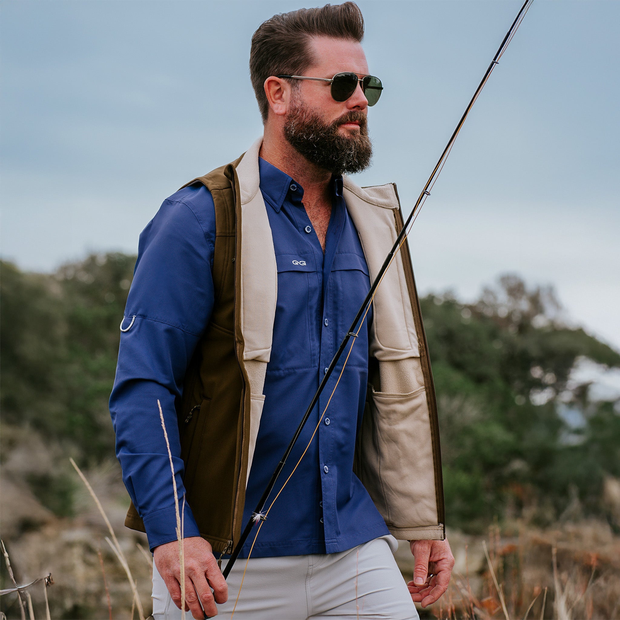 Man in outdoor setting wearing a blue shirt, beige vest, and sunglasses.
