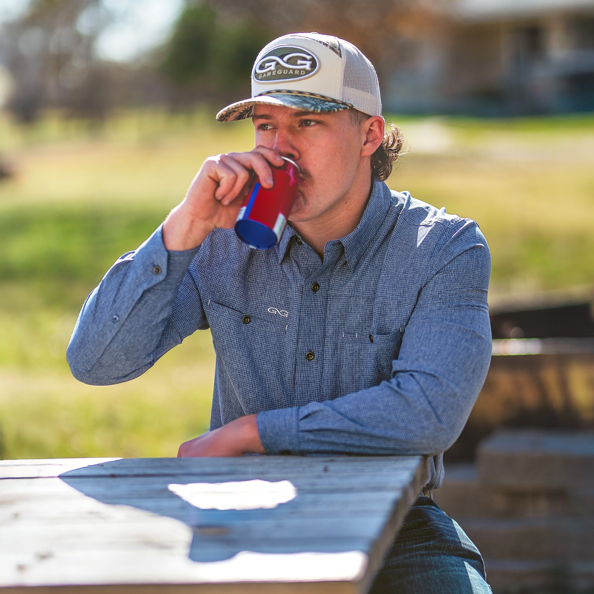 Man drinking from a red cup at a picnic table outdoors