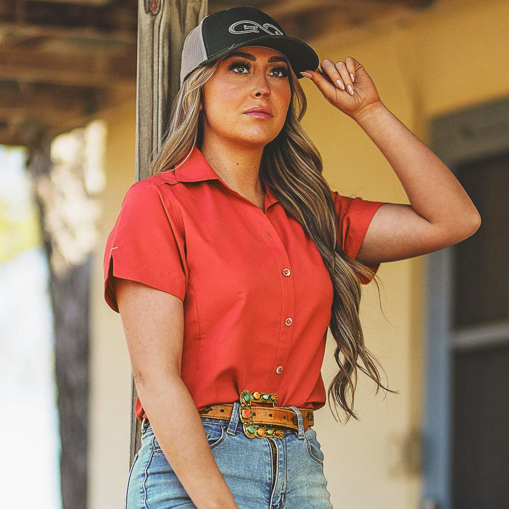 Woman wearing a red shirt, blue jeans, and a cap with a blurred background