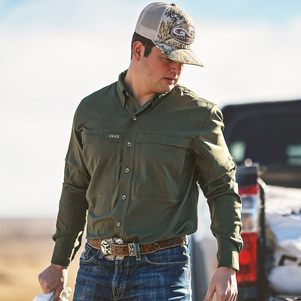 Man wearing a green shirt and camouflage cap with a truck in the background