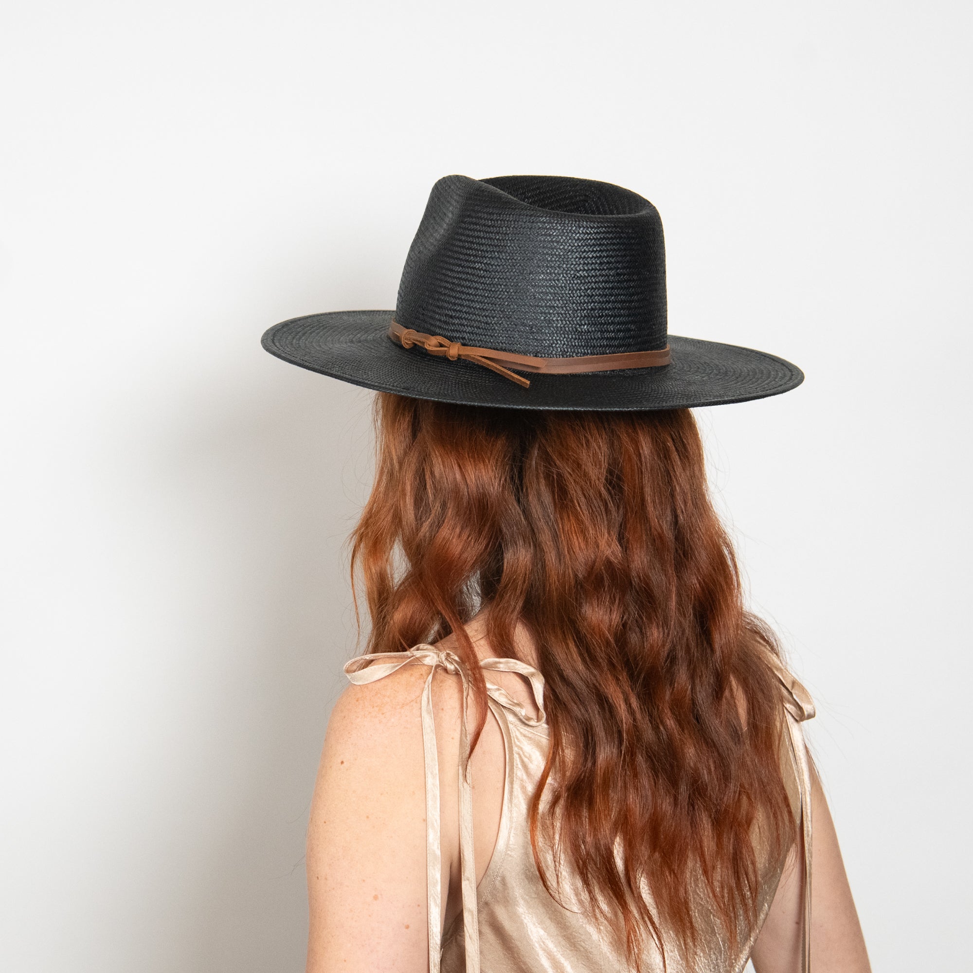 Person wearing a black fedora hat with a brown band on a plain background
