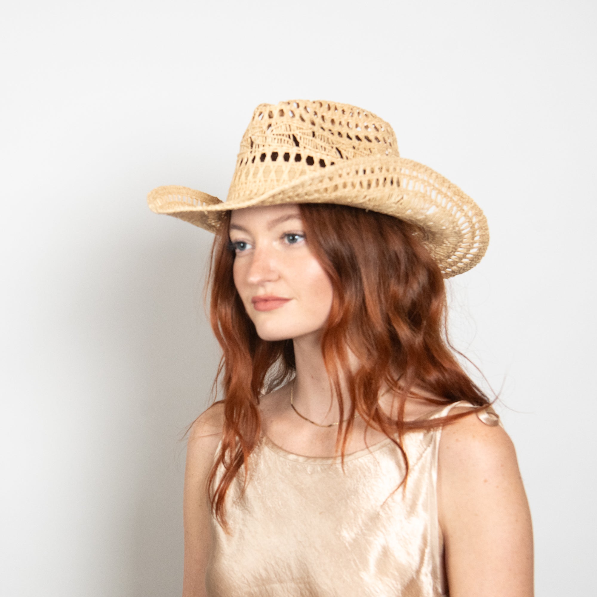 Woman wearing a straw cowboy hat against a plain background
