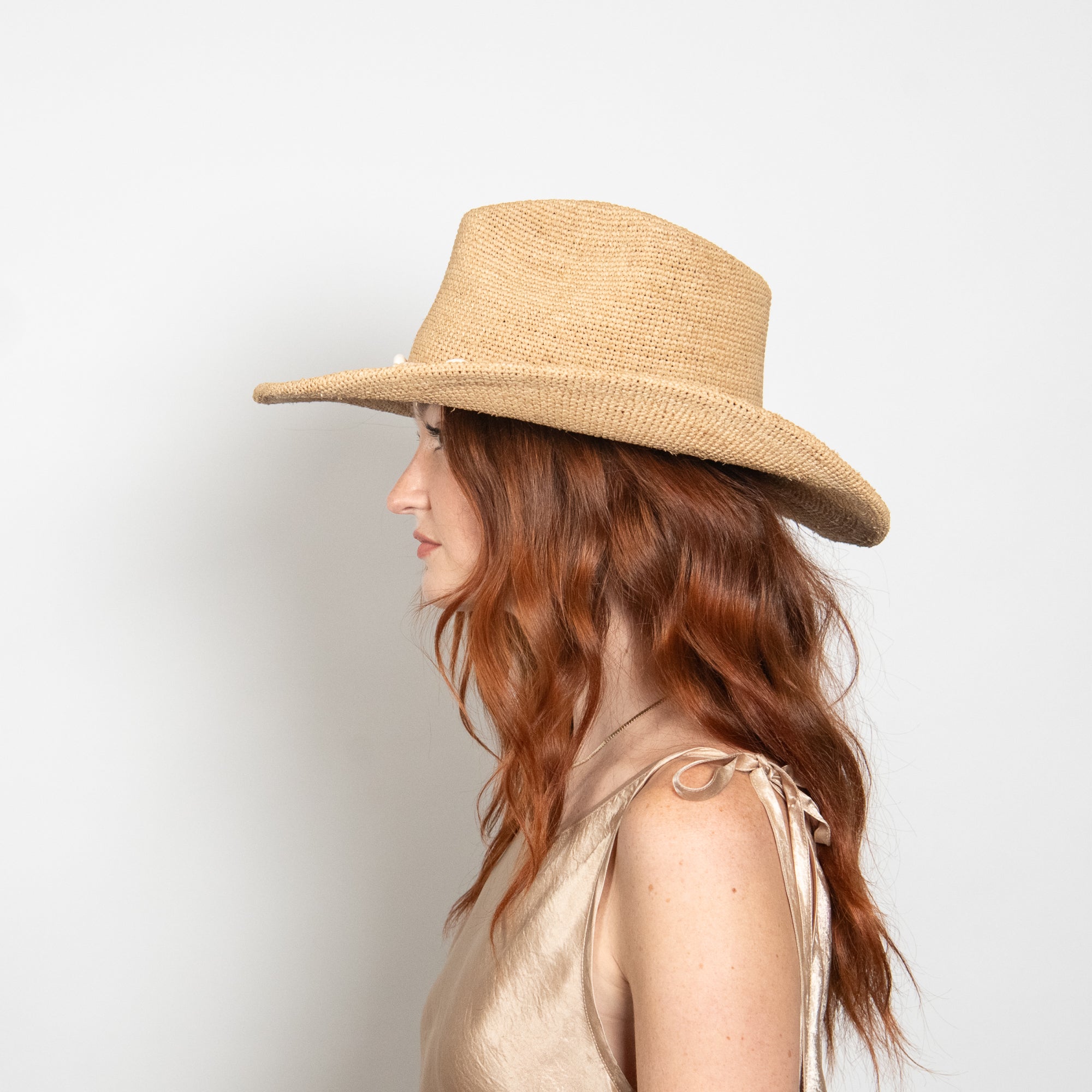 Woman wearing a beige straw hat against a light background