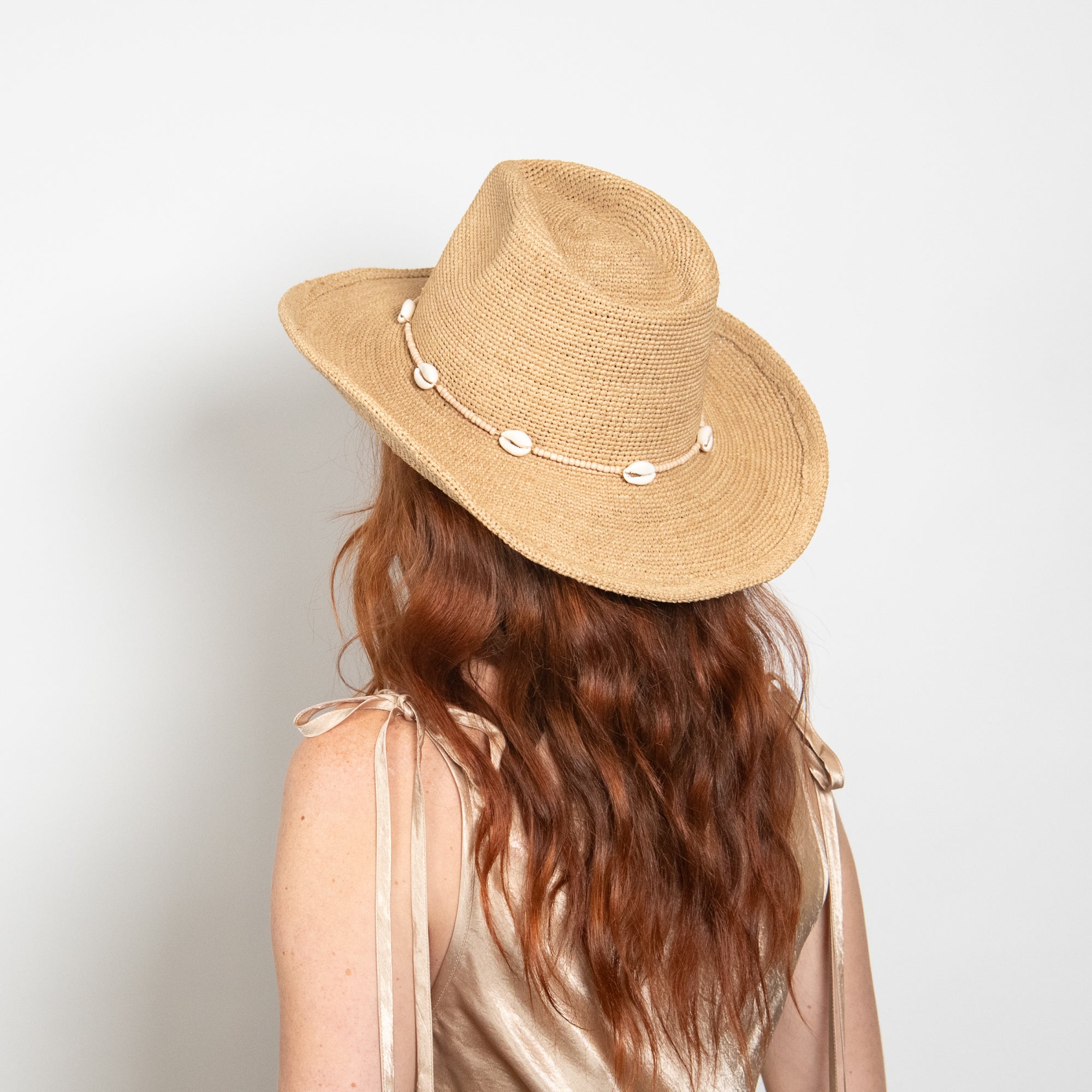 Person wearing a straw hat with decorative elements on a plain background