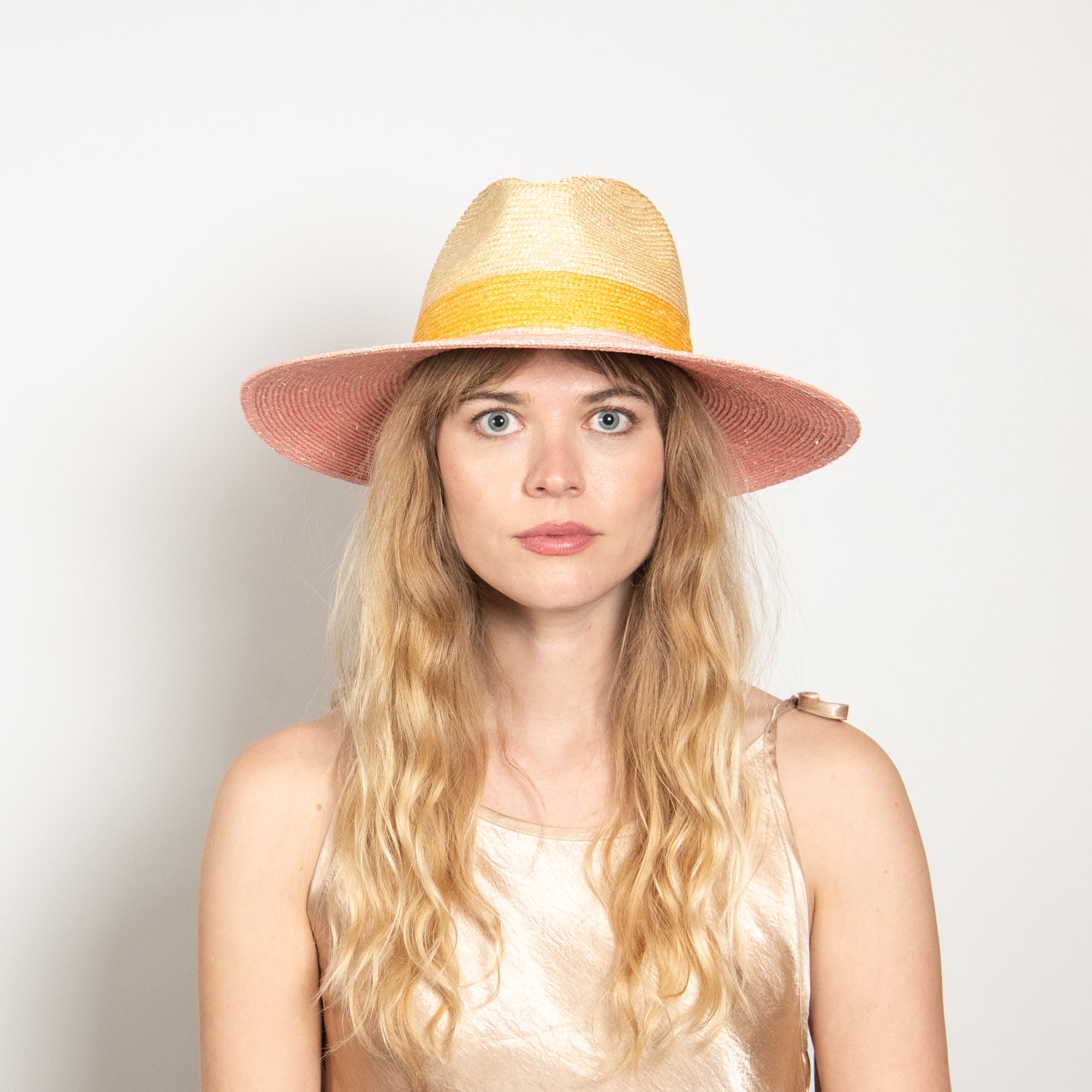 Woman wearing a wide-brimmed straw hat with a yellow band on a plain background